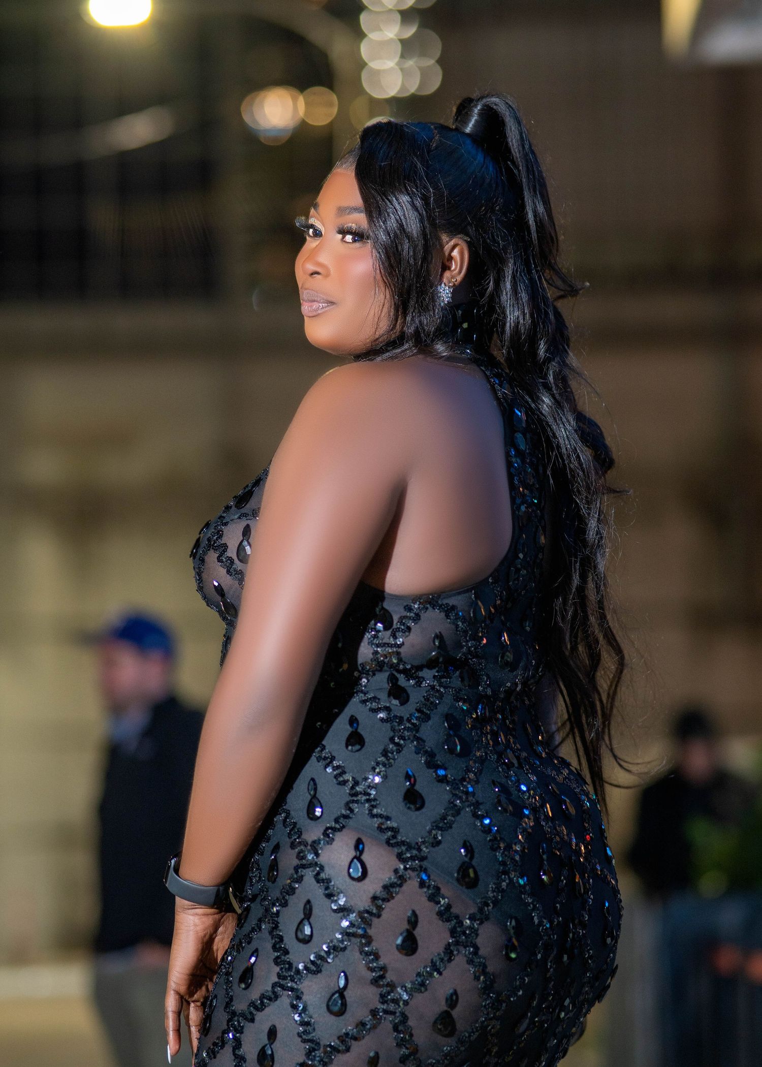 Woman in a sparkling black evening gown with long dark hair poses at a formal event.
