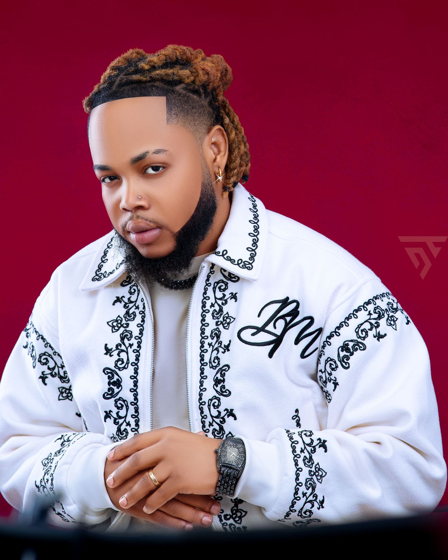 Stylish portrait in white embroidered jacket with black details against burgundy background.
