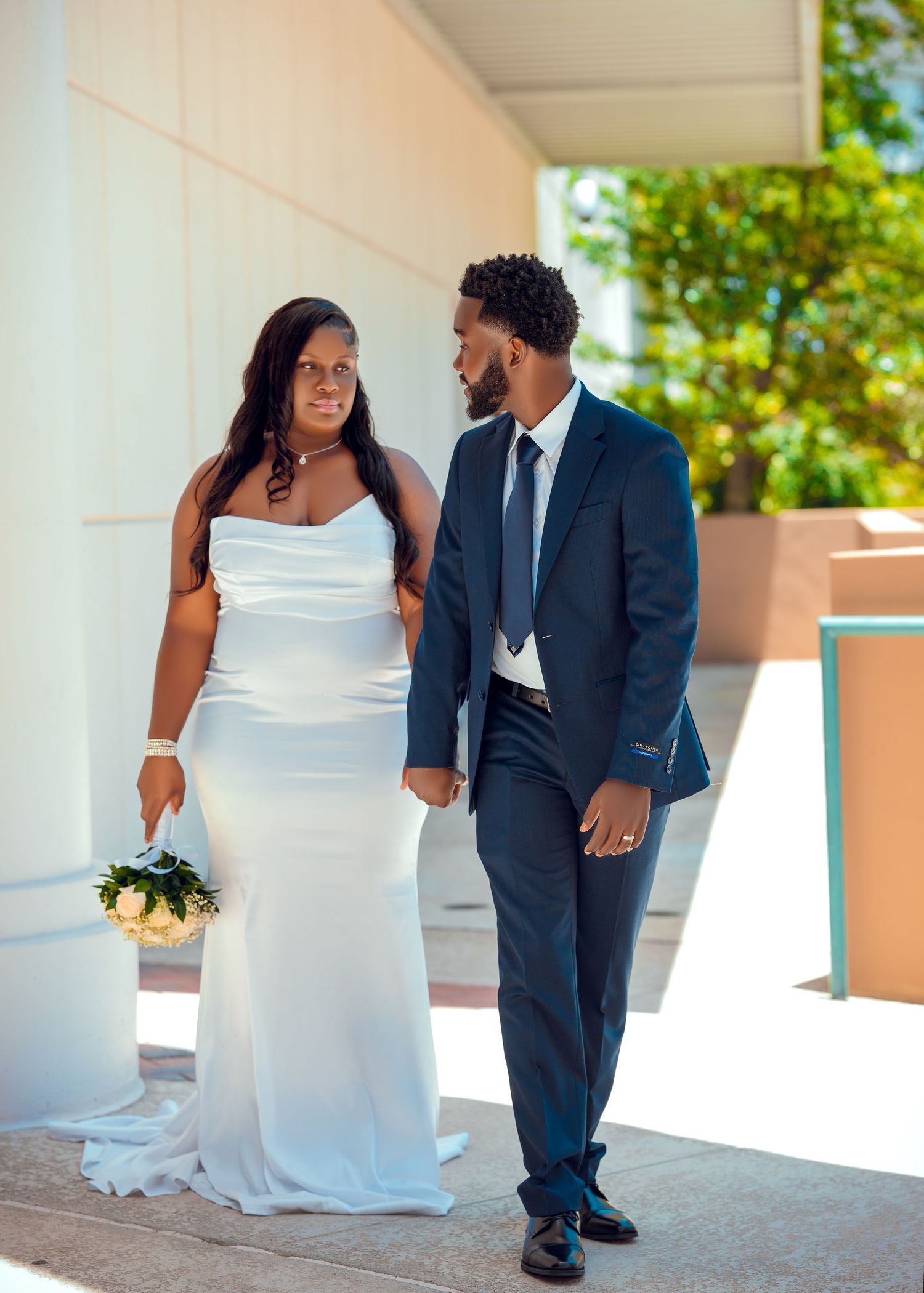Wedding portraits under white columns showcase couple in navy suit and flowing white dress.
