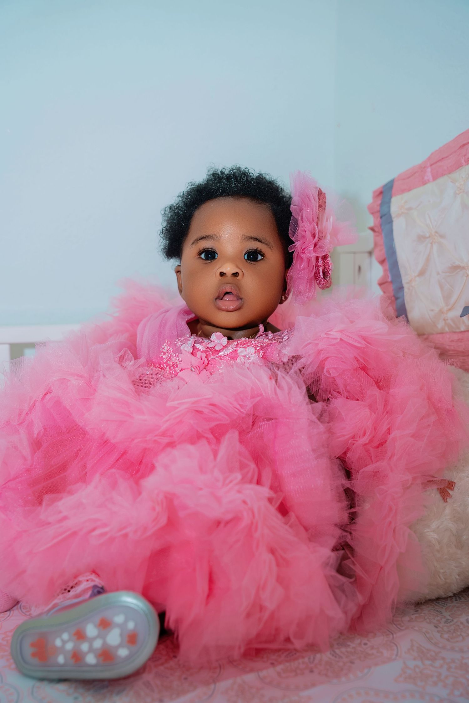 A baby wearing a fluffy pink tulle dress lies on a light blue background.
