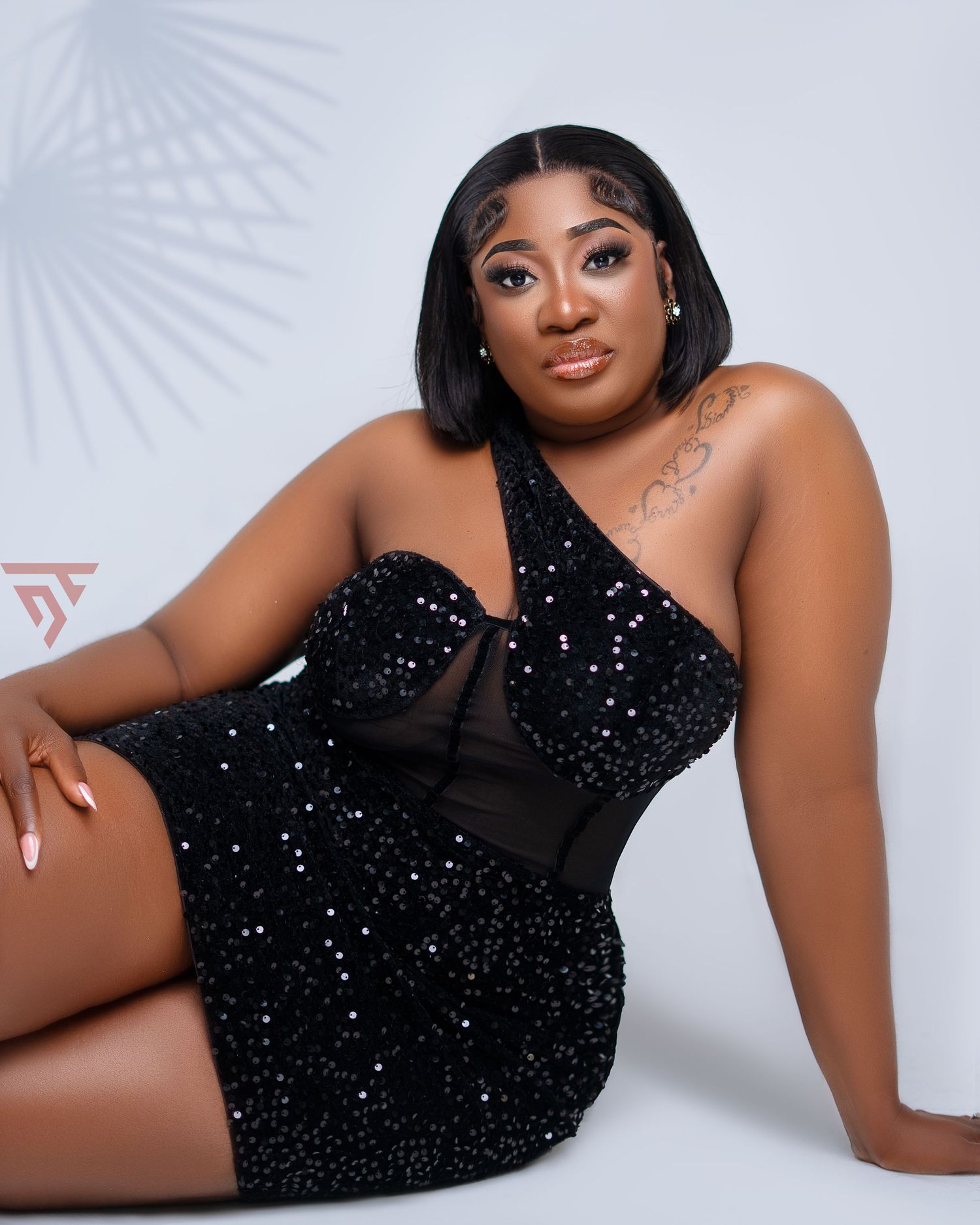 Glamorous pose in sparkly black dress against white studio background.