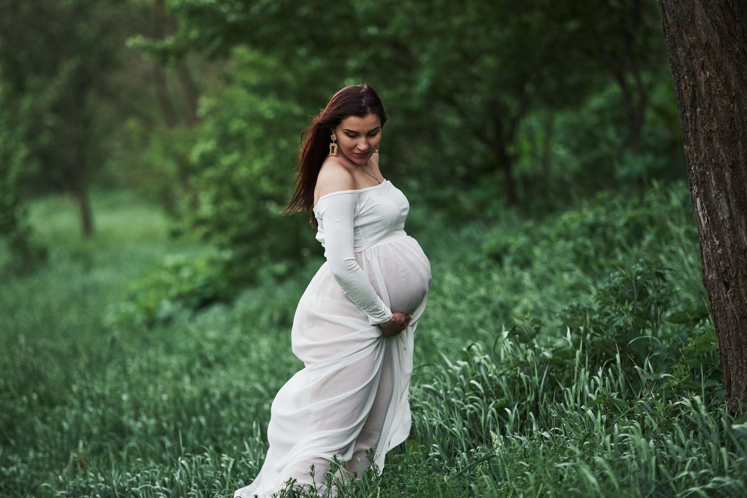 Natural outdoor maternity photos in white dress among green forest scenery.