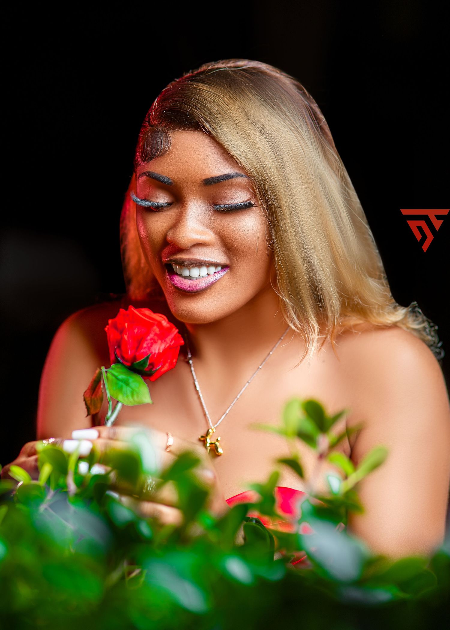 Portrait of someone with blonde hair holding a red rose against dark background with soft lighting.