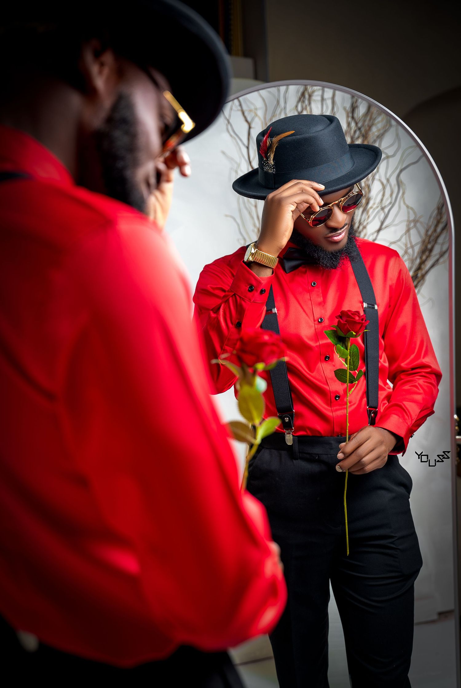 Reflection in mirror shows person wearing red shirt and black hat in artistic portrait.