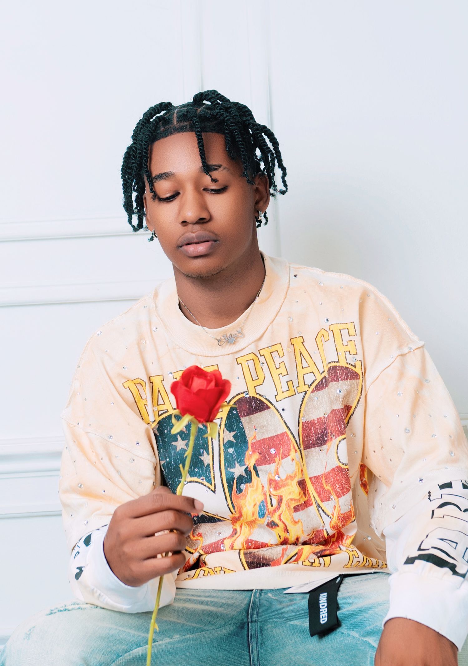 Person in peach colored graphic t-shirt holding red rose against white background.