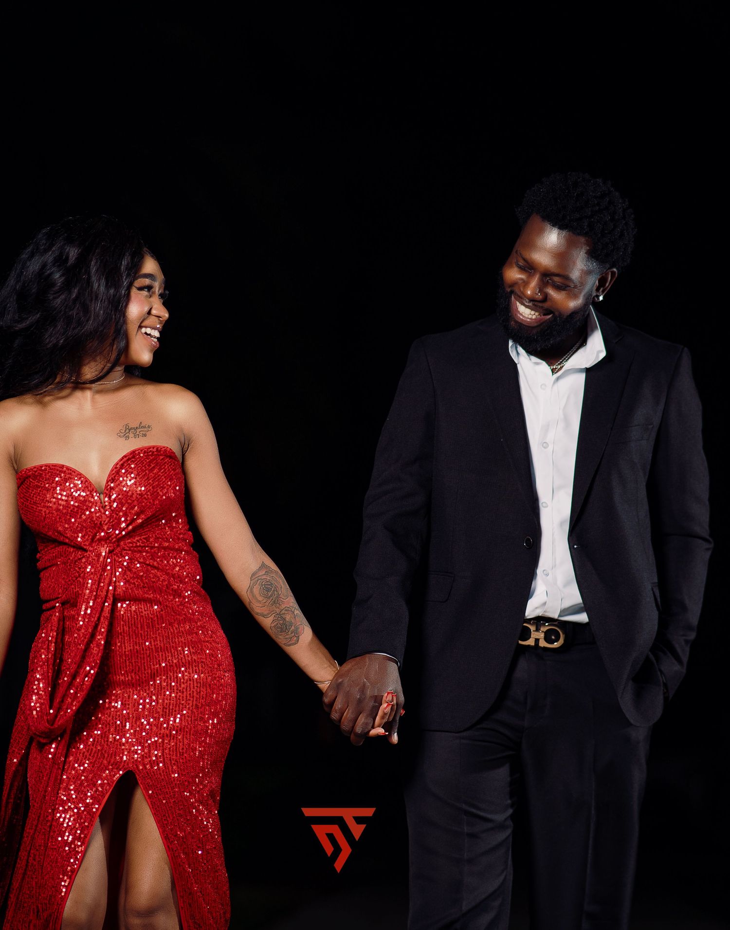 Couple in formal wear, with red sequin dress and black suit, sharing a romantic moment.
