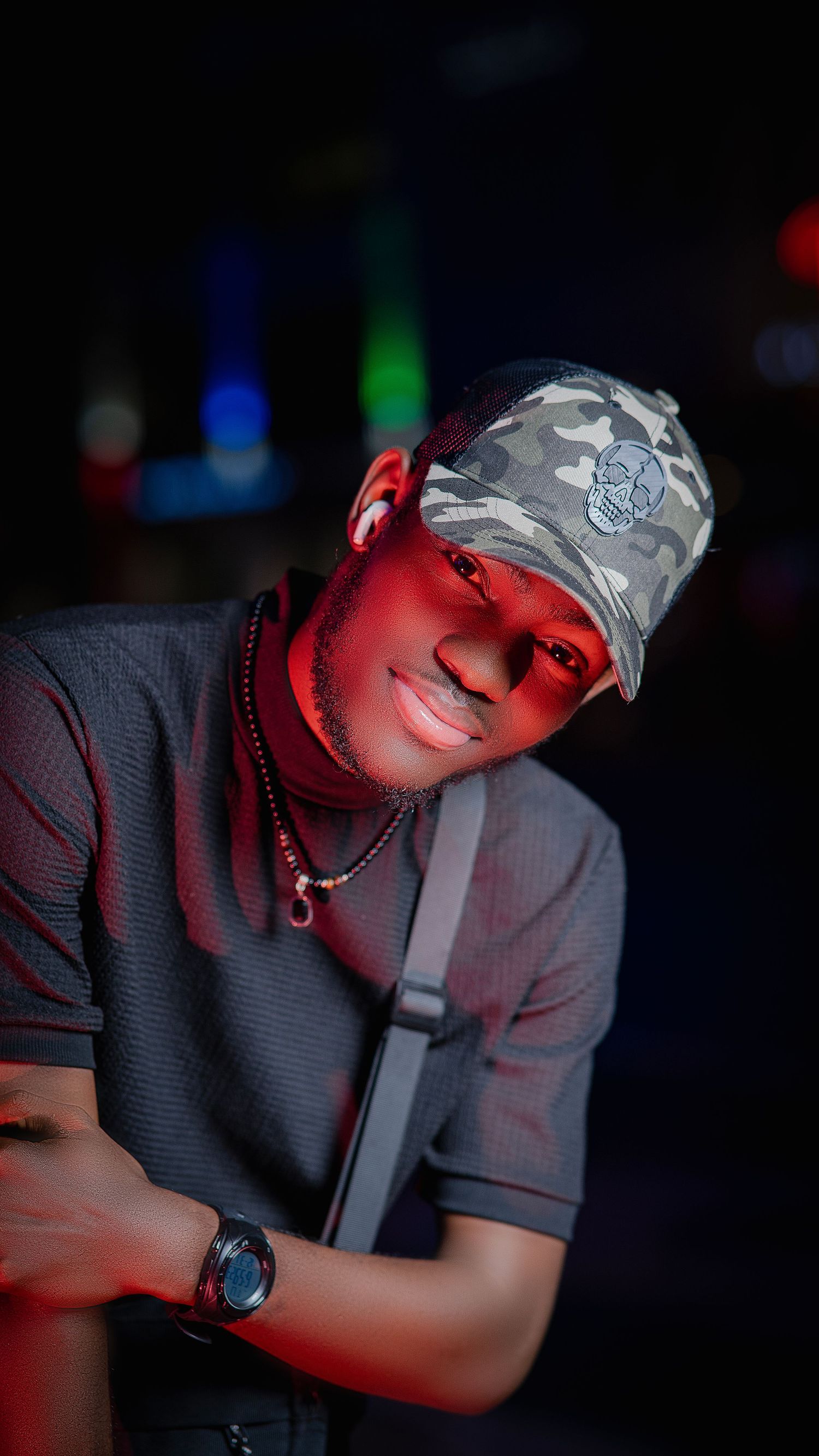 Artistic portrait with camo cap and dark shirt under dramatic red lighting.