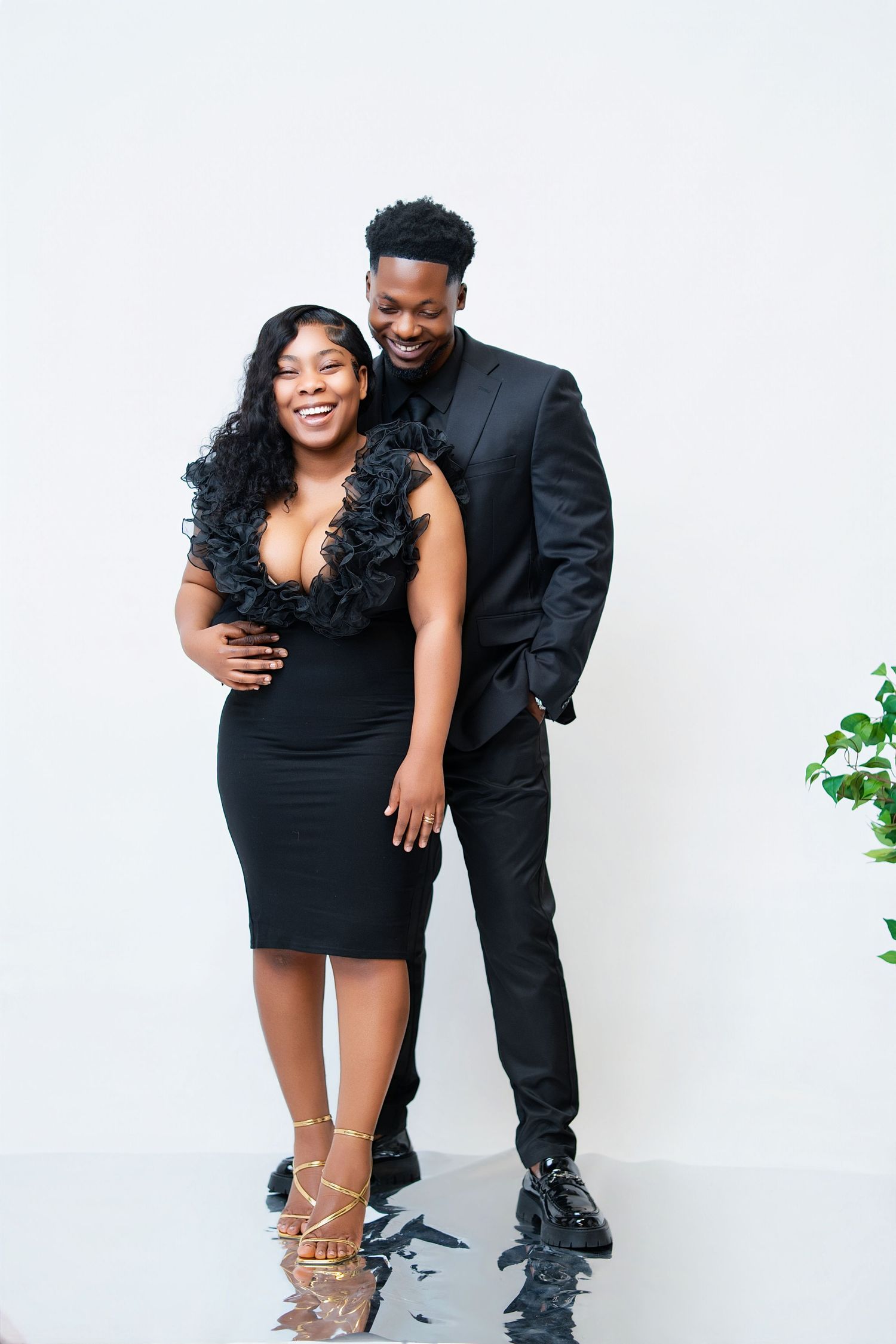 A smiling couple dressed in elegant black formal attire poses together against a white background.