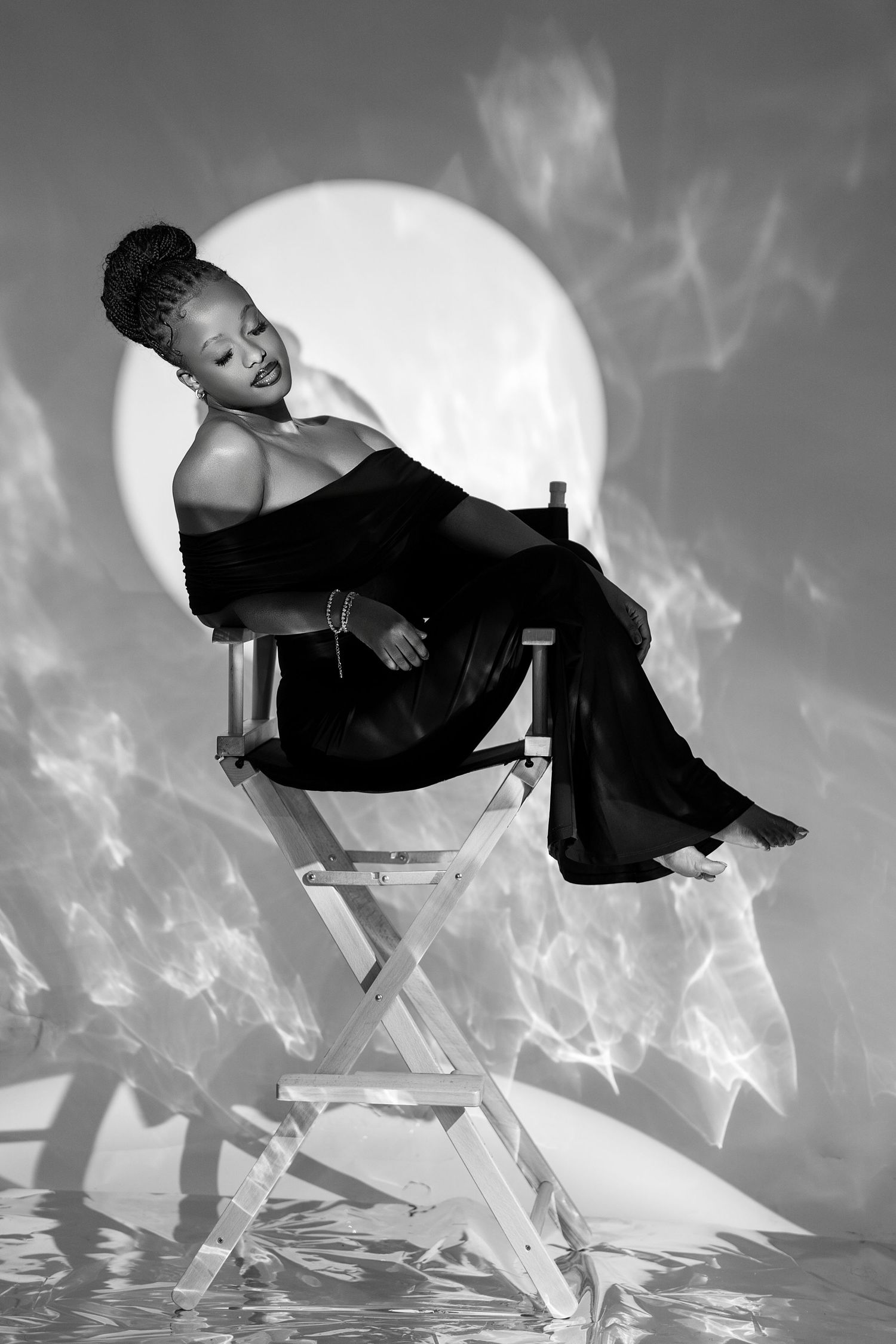 Black and white photo of a woman in elegant black outfit seated on a director's chair with a glowing moon backdrop.