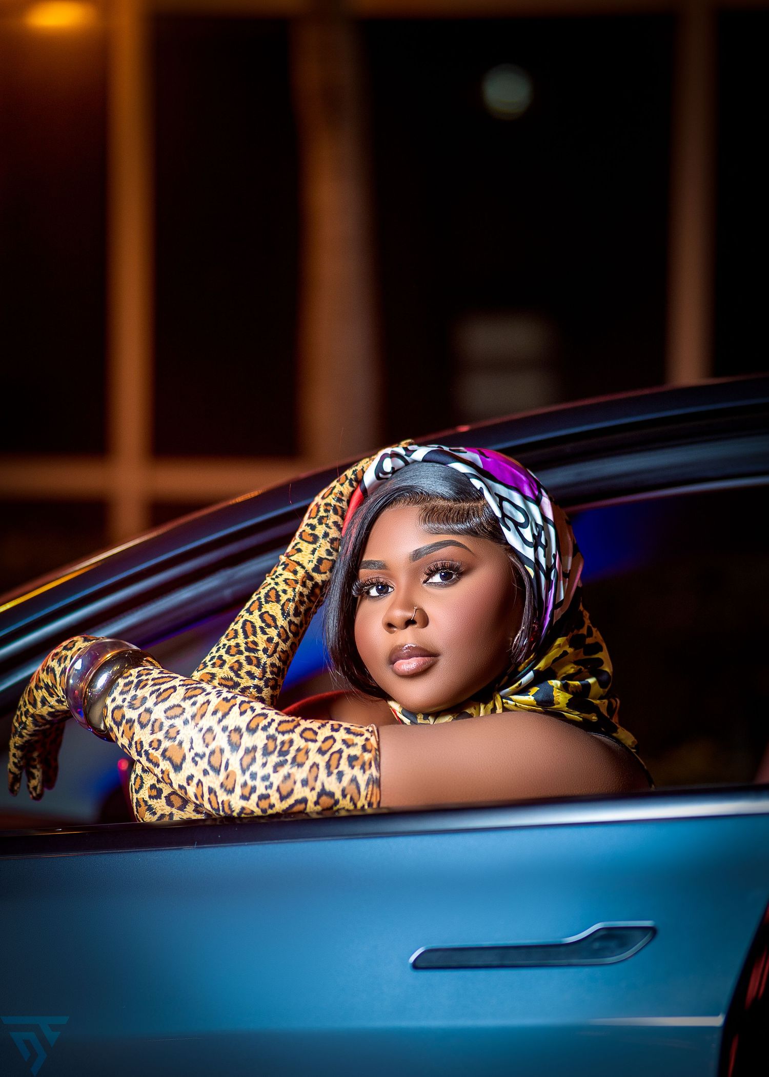 A person in a leopard print outfit poses through a car window at night with dramatic lighting and shadows.
