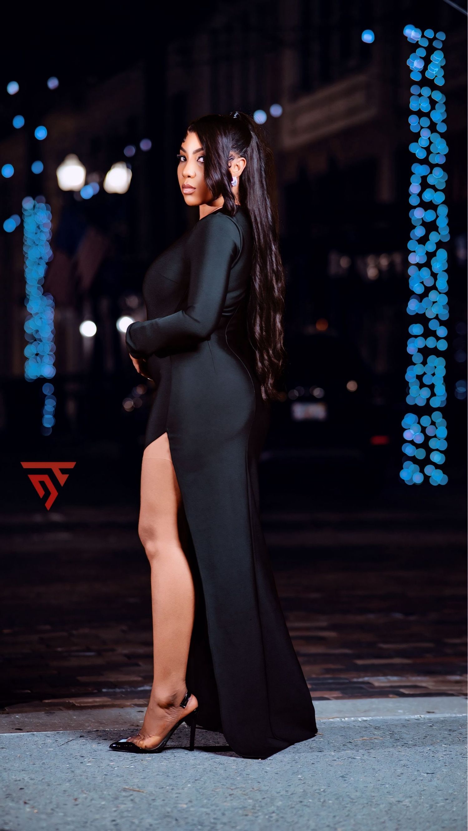 Elegant black evening gown with high slit photographed at night with blue lights.