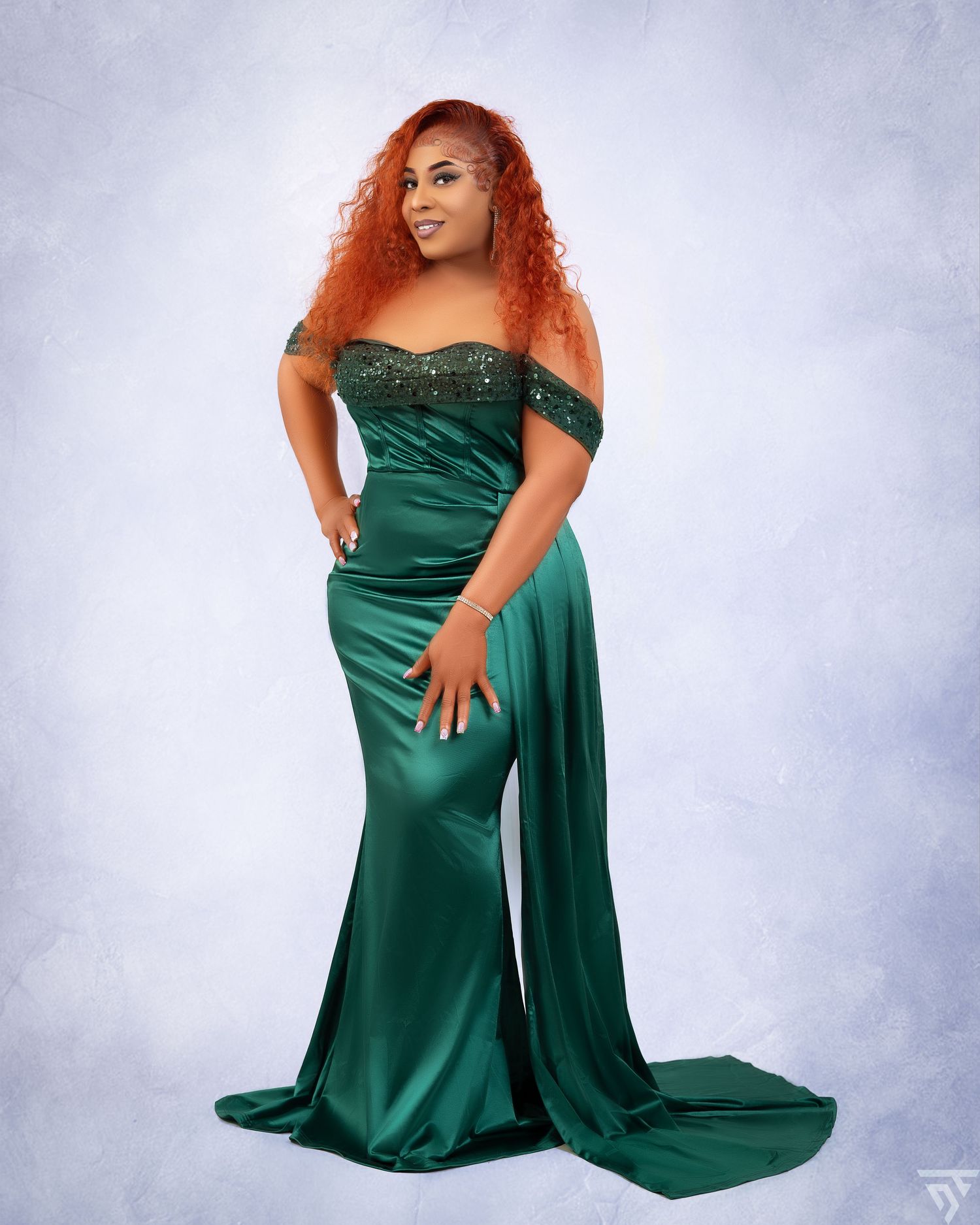 Flowing emerald green formal dress with sparkly details in studio setting.