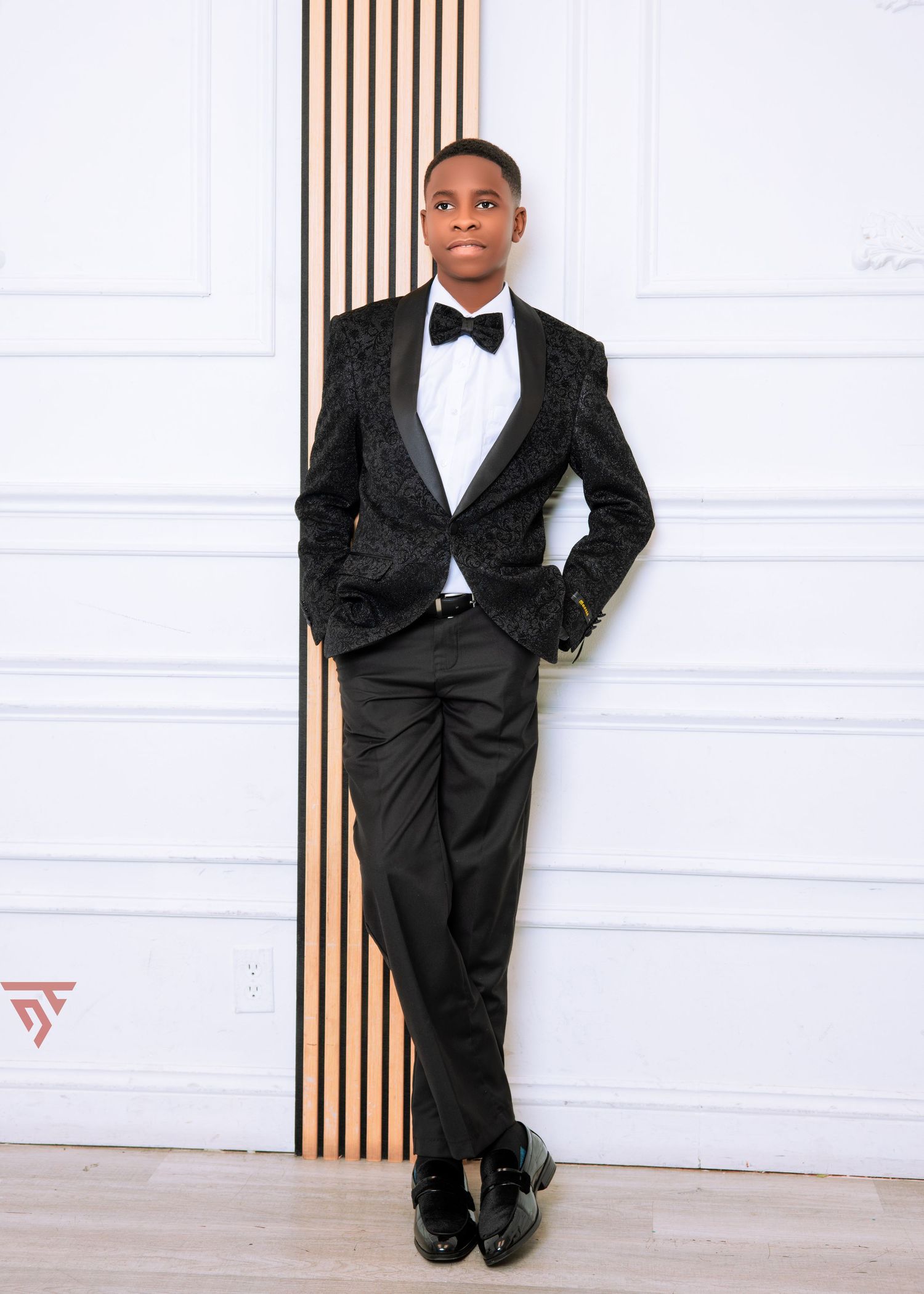 Professional portrait session in black tuxedo against white wall with wood accent panels.