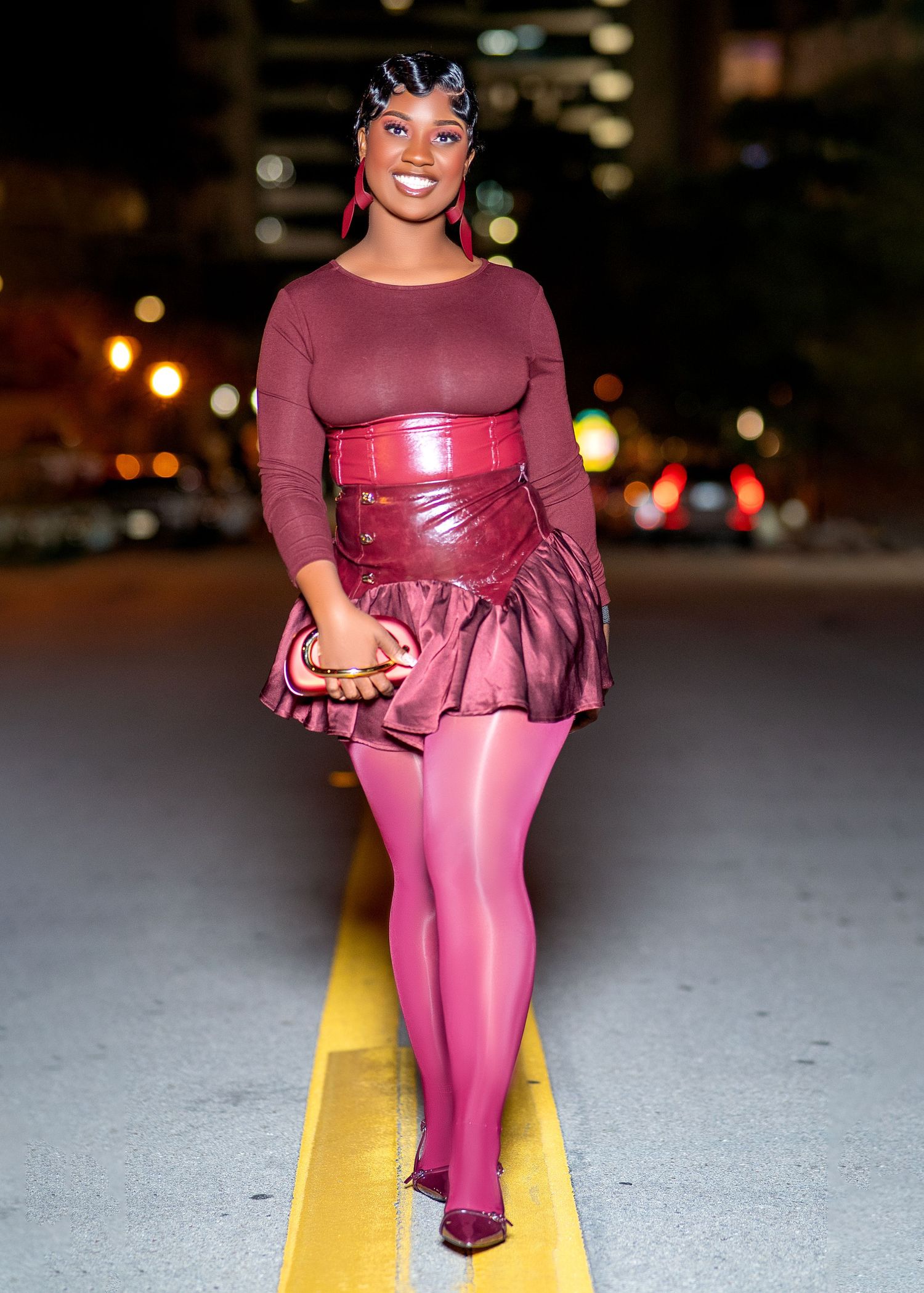 Person wearing burgundy ensemble with pink accents poses on yellow line at night.