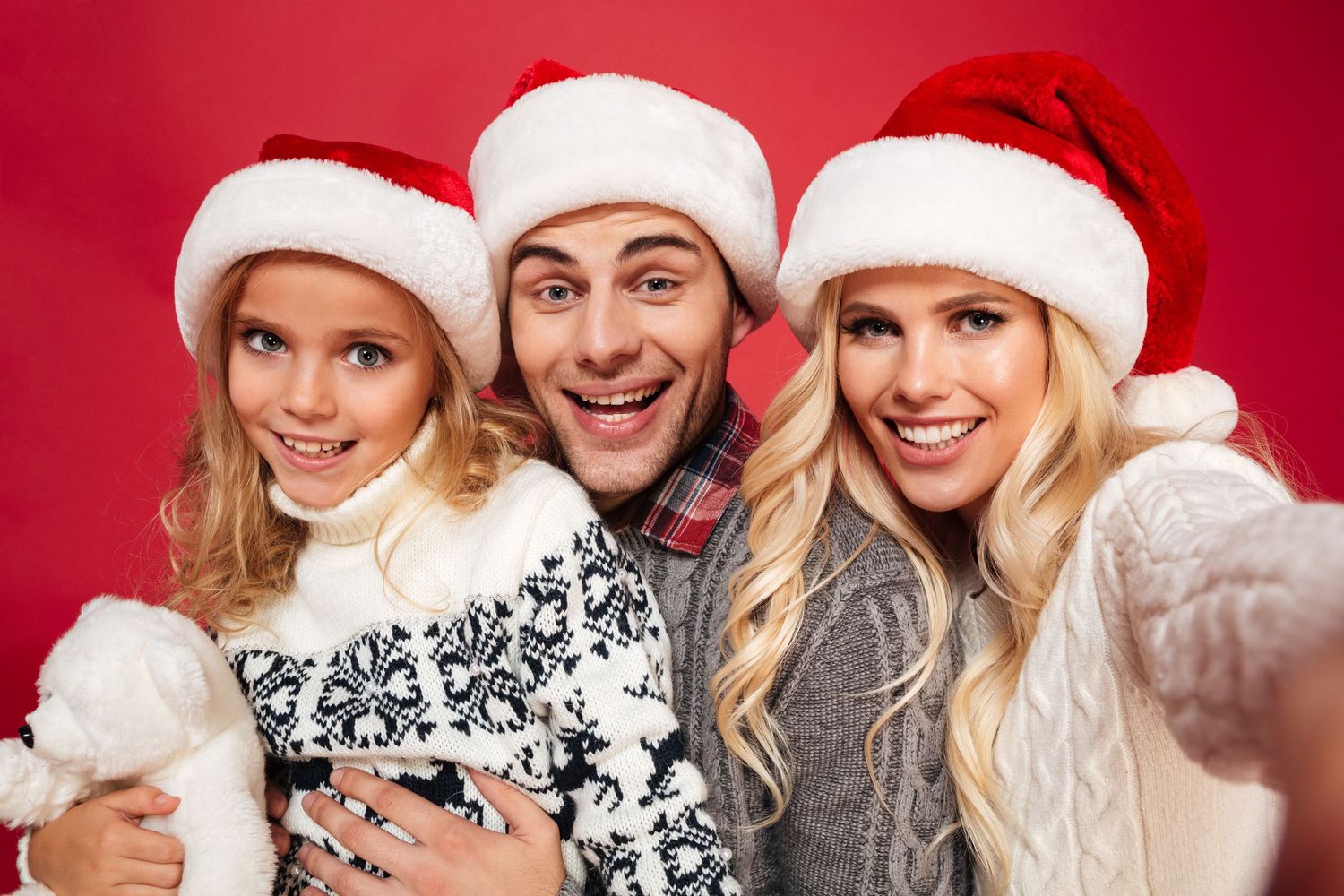Group wearing Santa hats and winter sweaters smiling together in festive holiday photo.