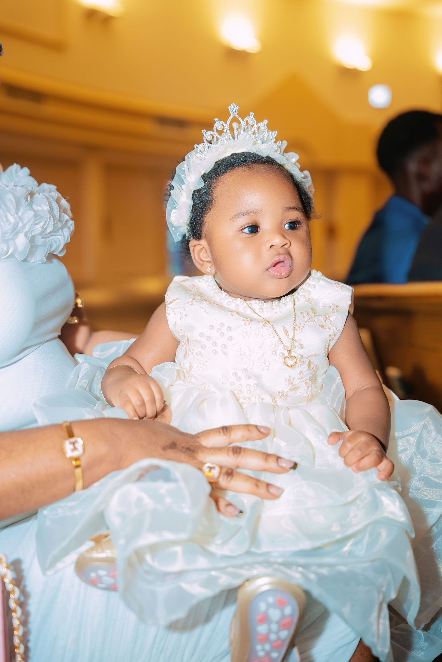 Baby wearing white dress and tiara during a special celebration or christening ceremony.