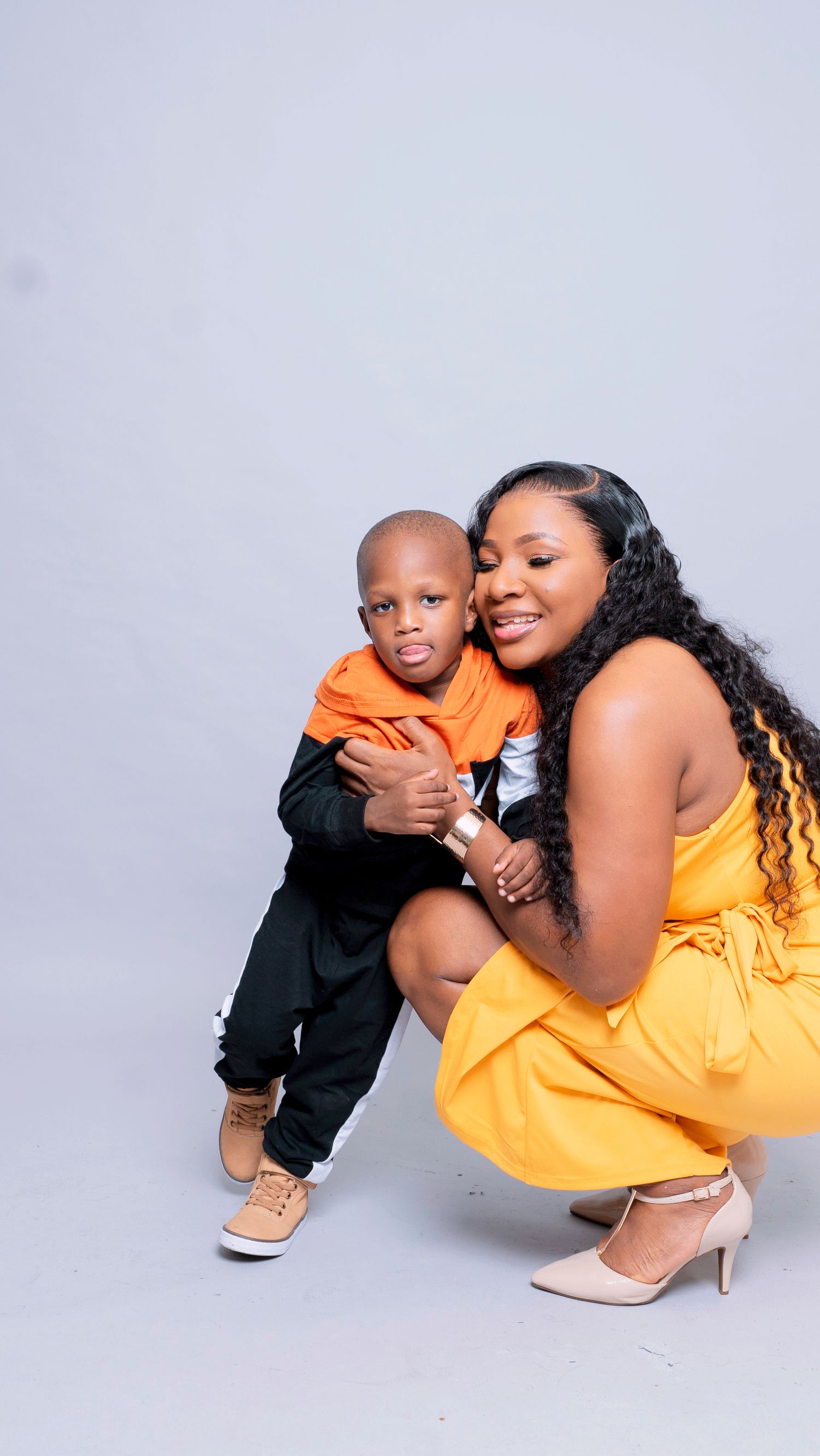 Portrait session with woman in yellow dress and child in black outfit against white background.