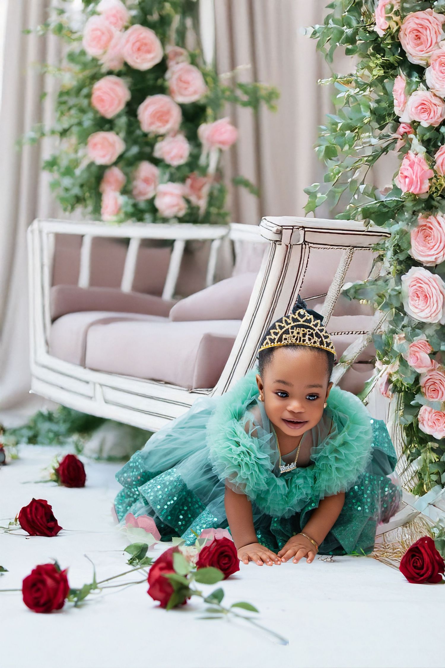 Young girl in teal princess dress and crown crawls on white floor surrounded by red roses and pink floral decor.
