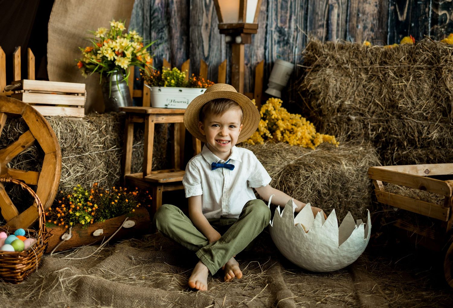 Child sits in rustic setting with hay bales and sunflowers in natural lighting.