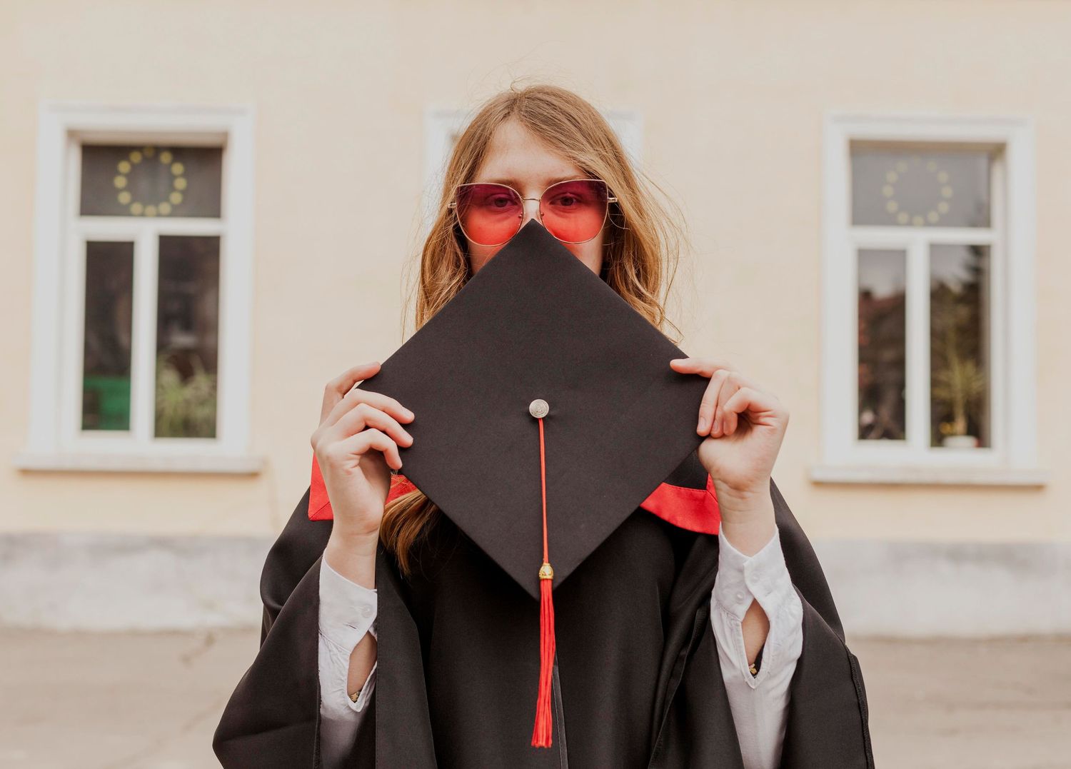 Graduate in black academic regalia poses with red accents on graduation day.