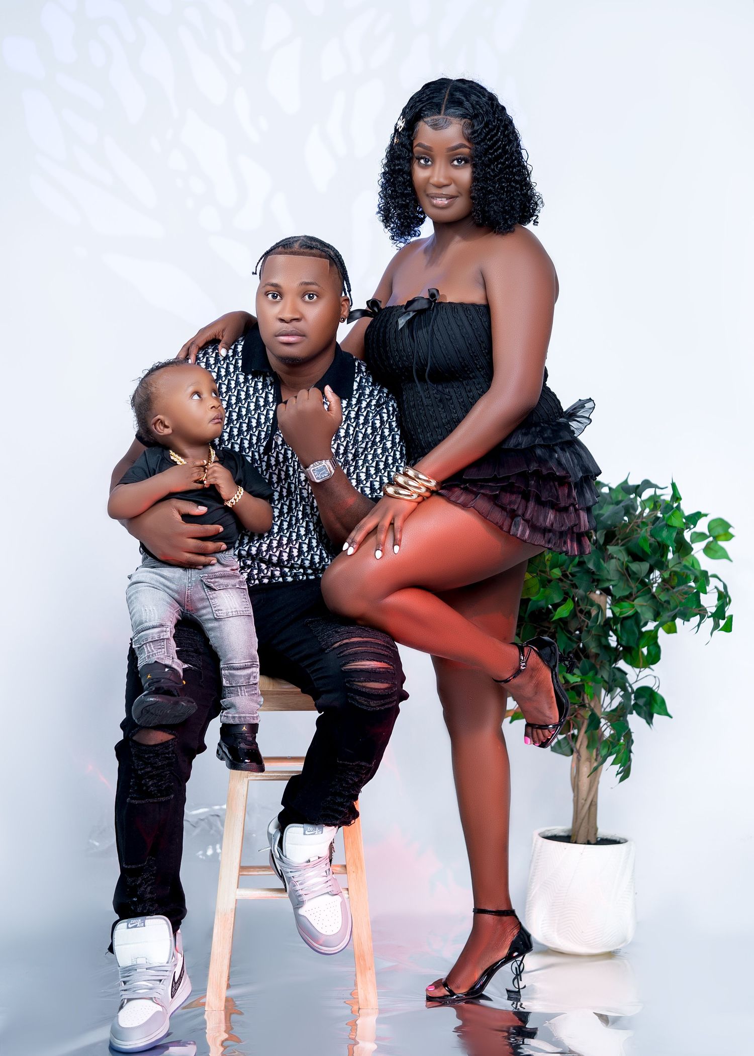 A family portrait of two adults and a toddler posing together in a bright studio setting.