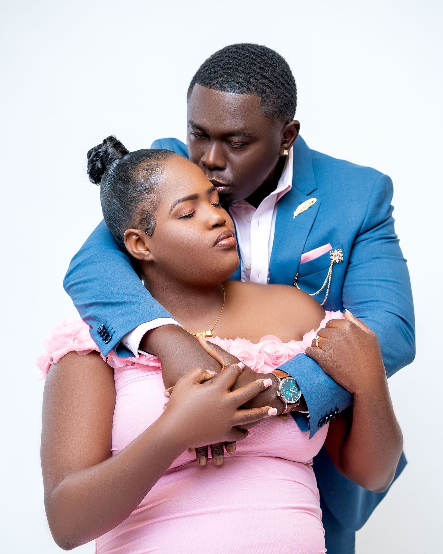 A couple in a romantic embrace, man in blue suit kissing woman in pink dress during a professional photo shoot.