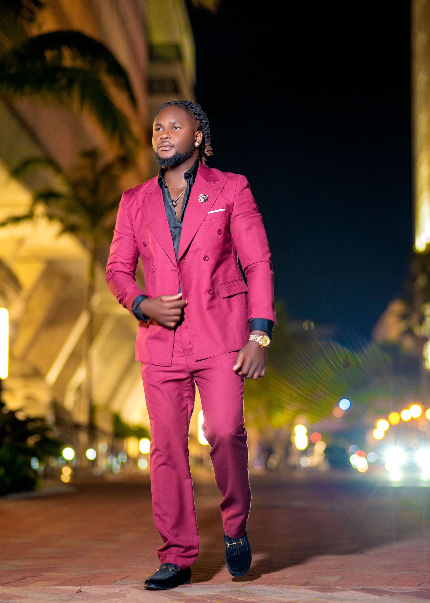 Man in a stylish magenta double-breasted suit posing confidently outdoors at night with city lights behind him.