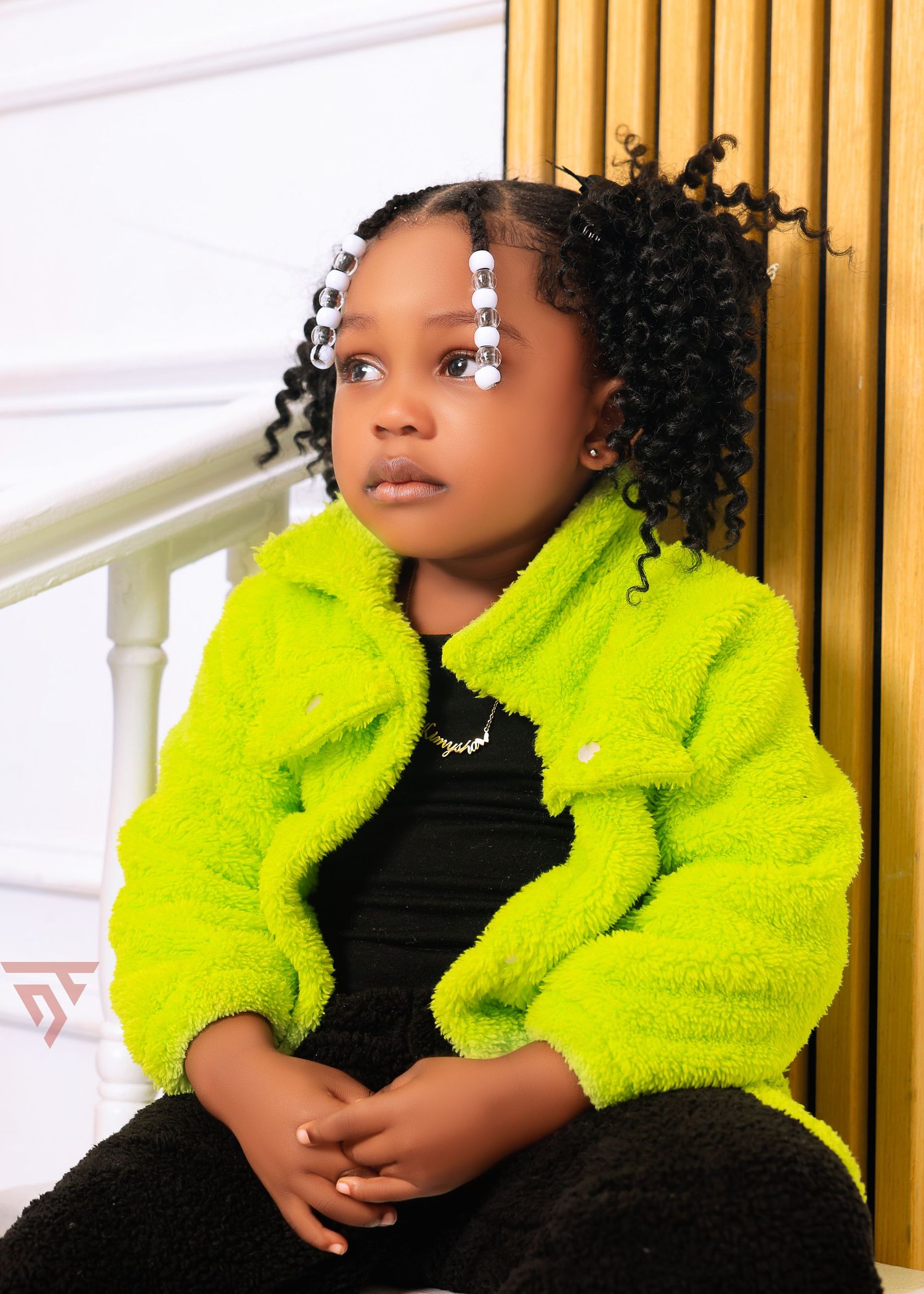 Child in fluorescent yellow fuzzy jacket poses against white wall with wooden vertical panels.
