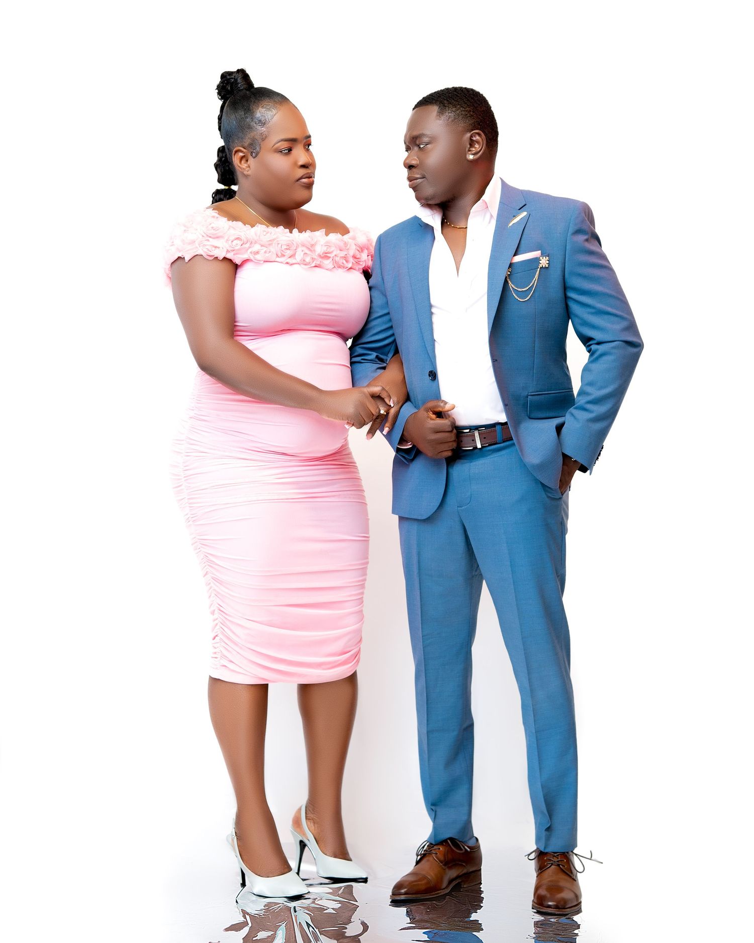 A couple poses elegantly, woman in pink dress and man in blue suit, against a white background.