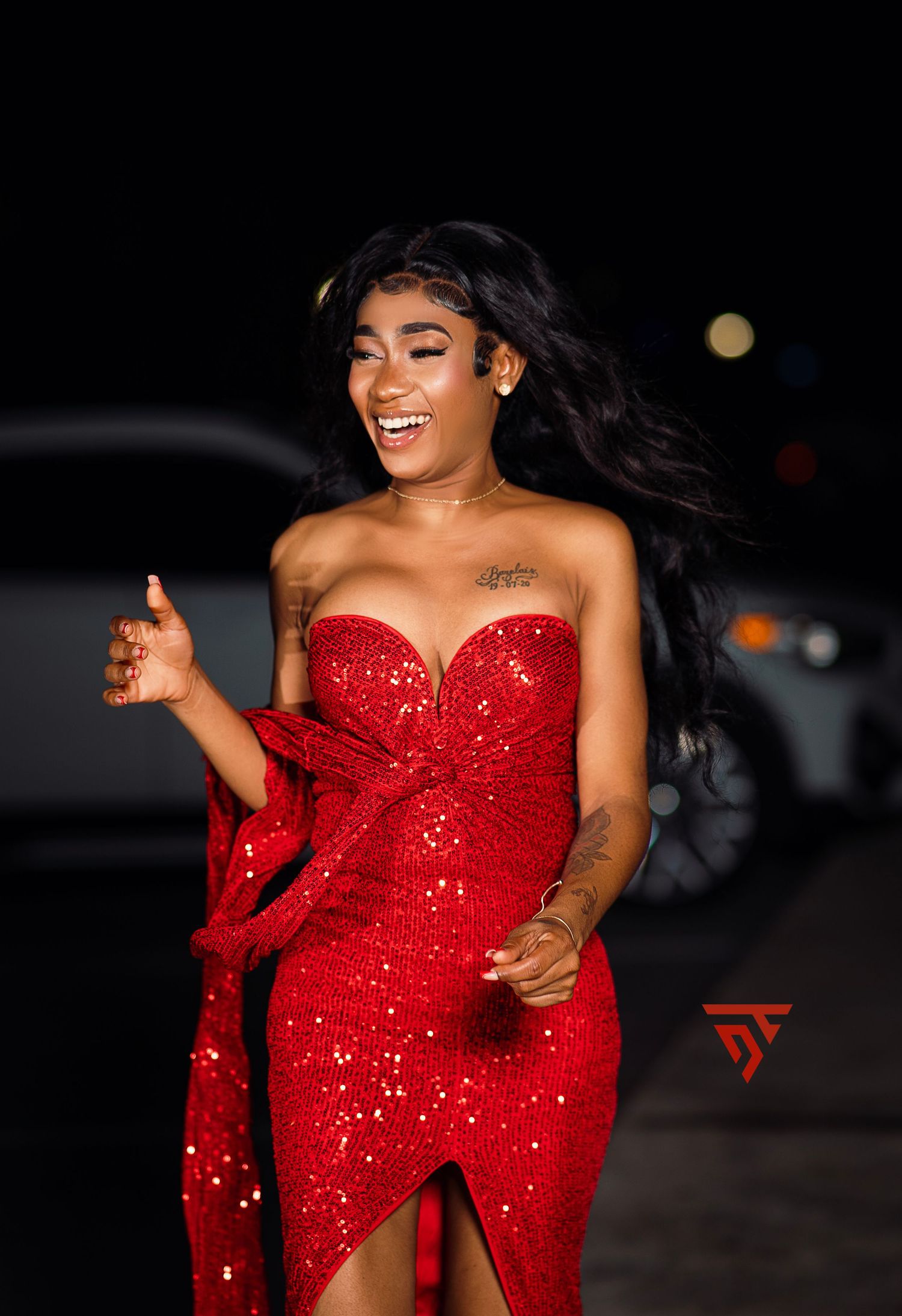 Person in sparkling red evening gown with slit poses outdoors at night.