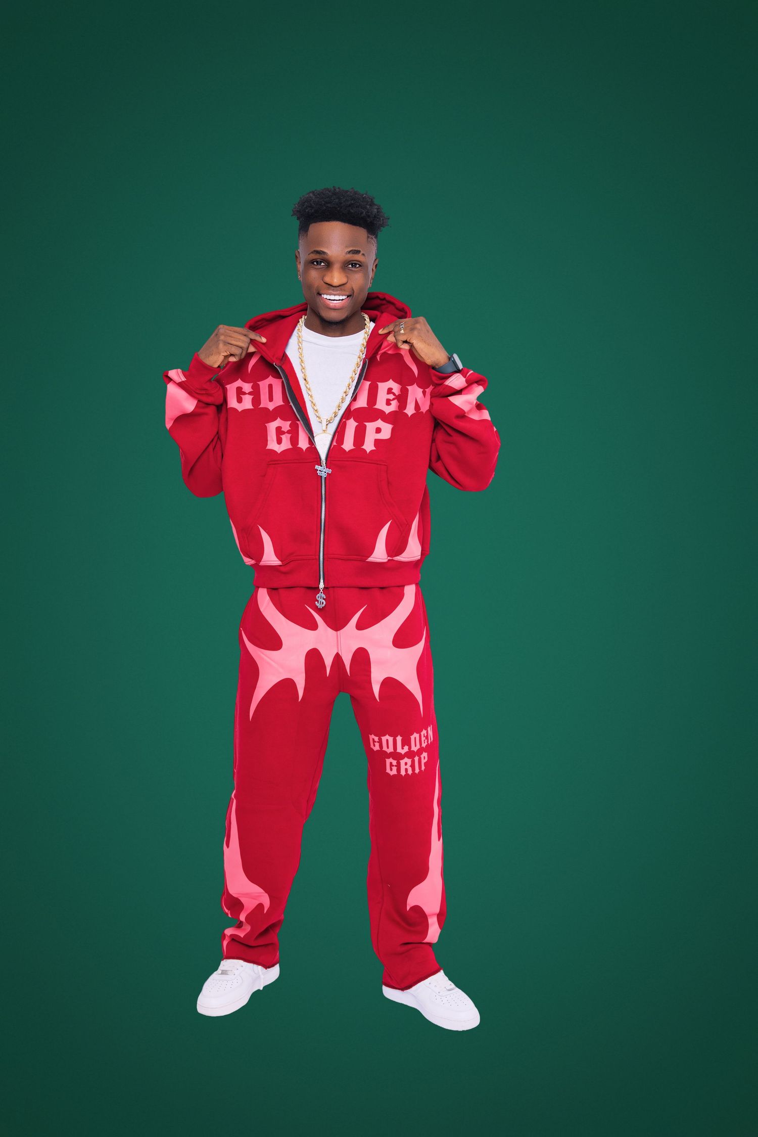 Person wearing a vibrant red and pink Golden Grip tracksuit poses against a dark green background.