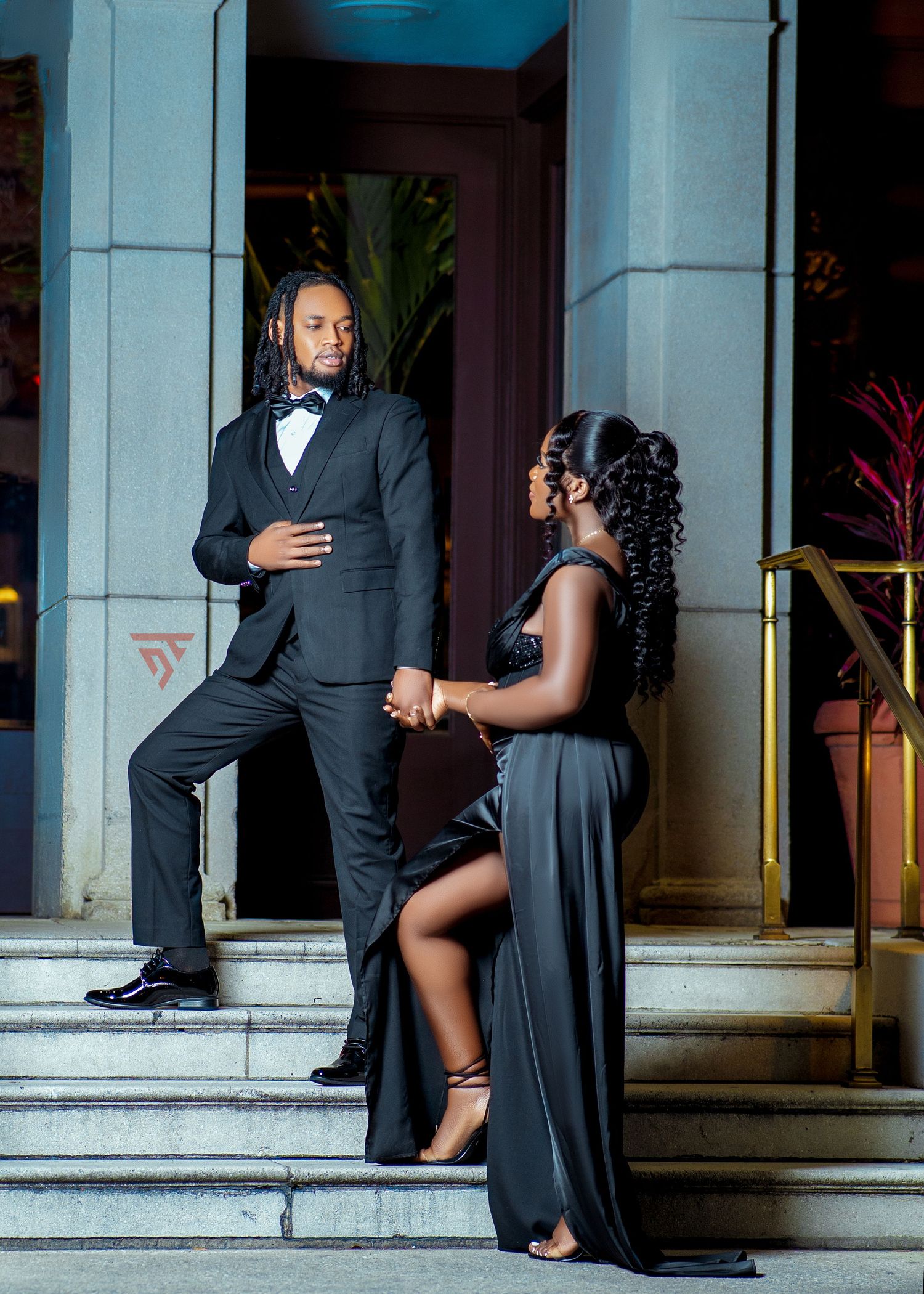 A couple poses on stone steps in formal evening wear for a romantic photoshoot.