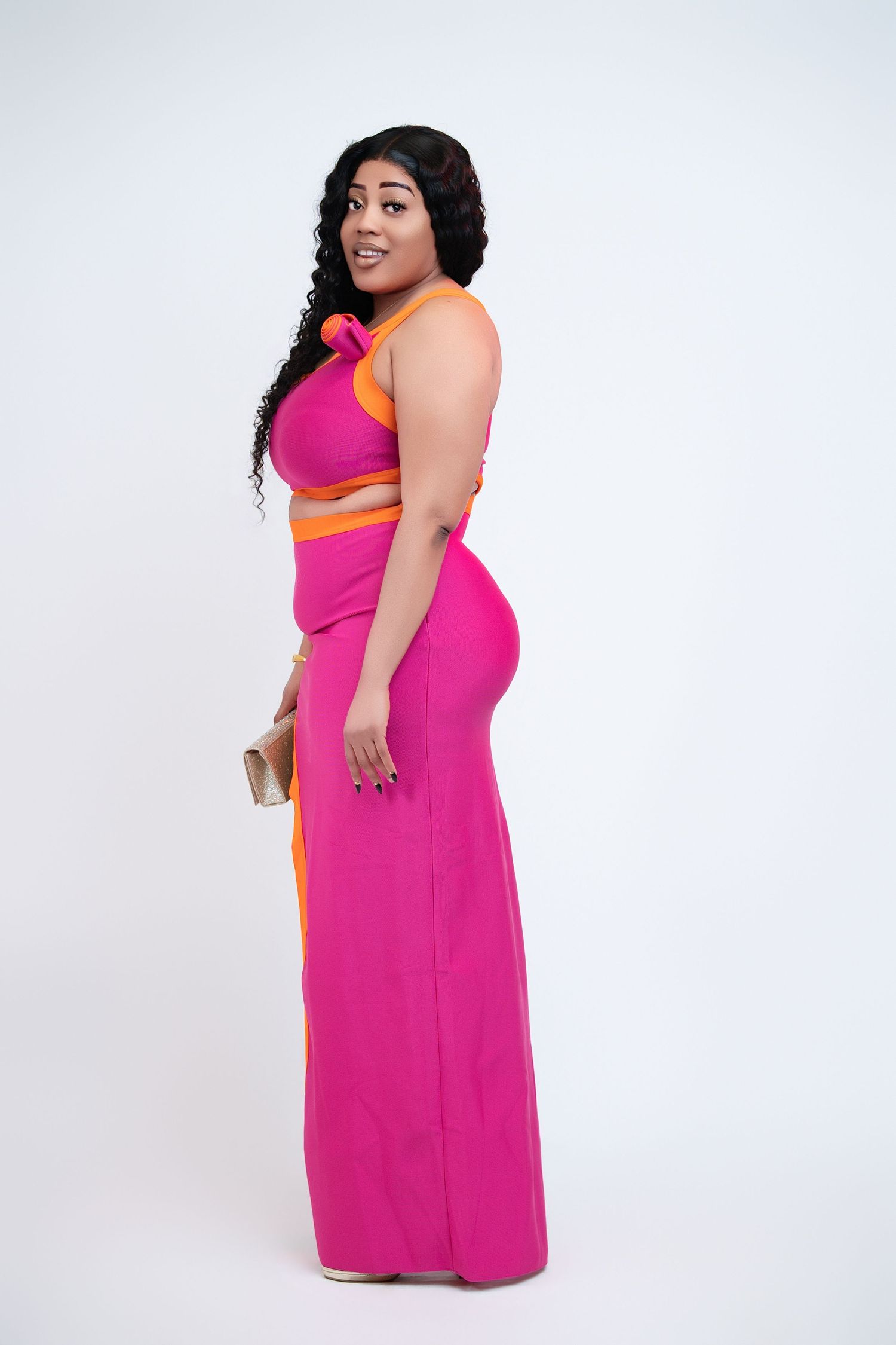 Woman in vibrant pink and orange two-piece halter outfit posing against white background.