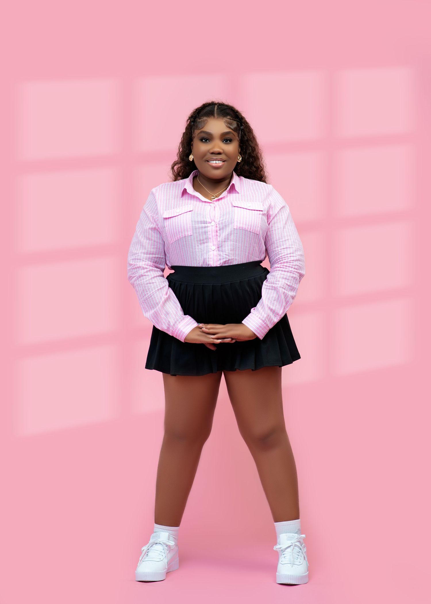Young woman smiling in pink striped shirt and black mini skirt, posing against a pink background.