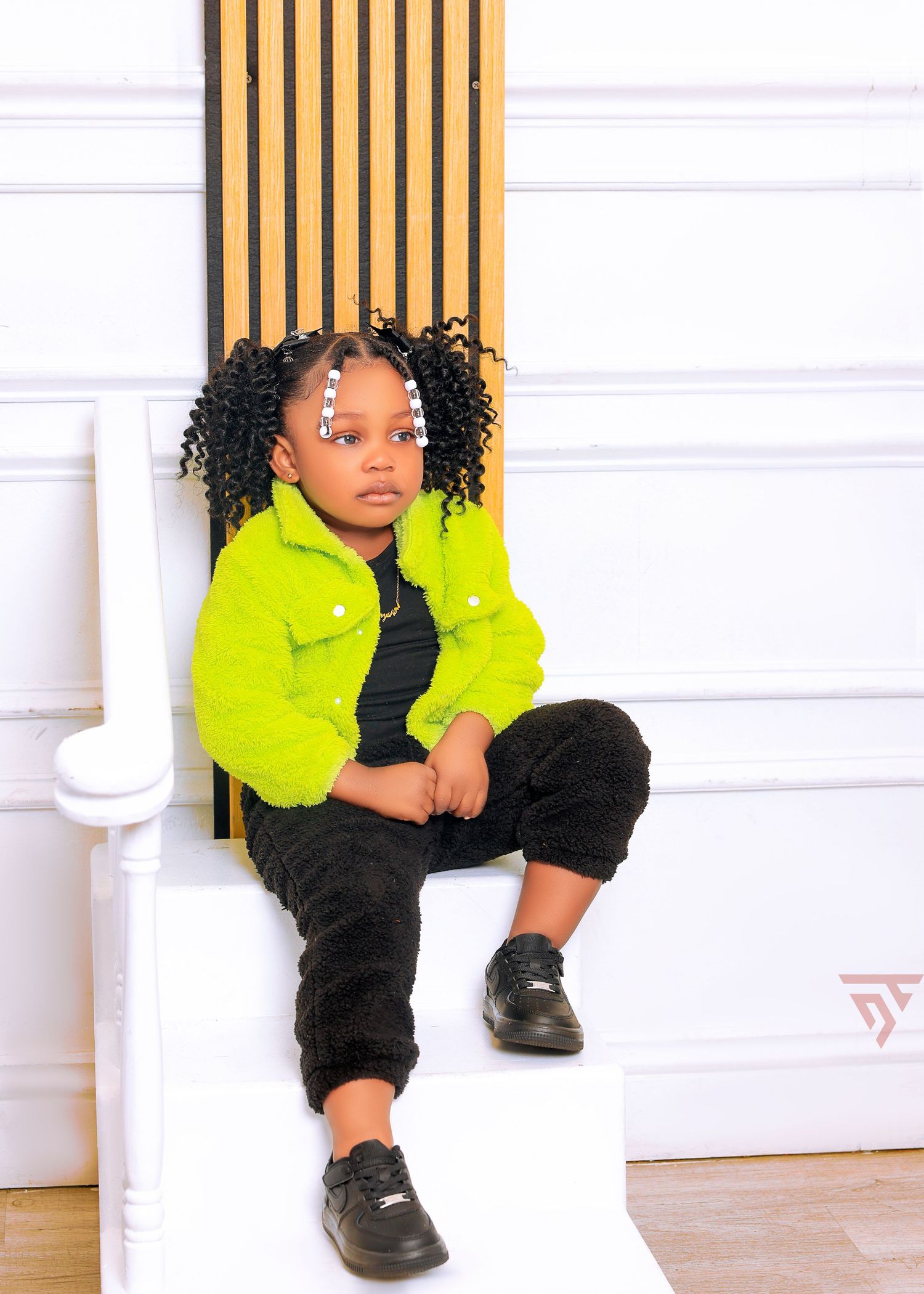 Child wearing bright yellow jacket and black outfit poses near white wall with wooden accents.