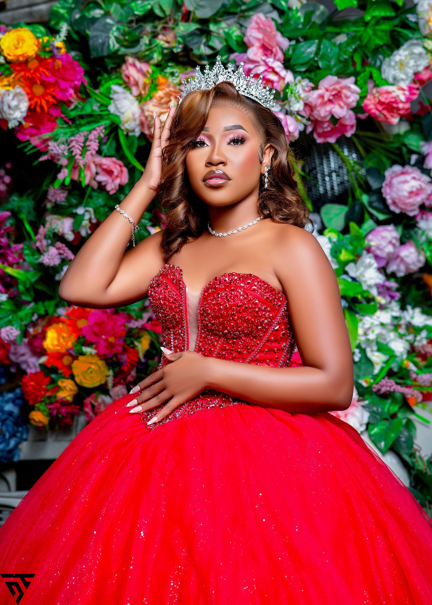 A stunning red ball gown with beaded bodice against a floral backdrop with pink and yellow roses.