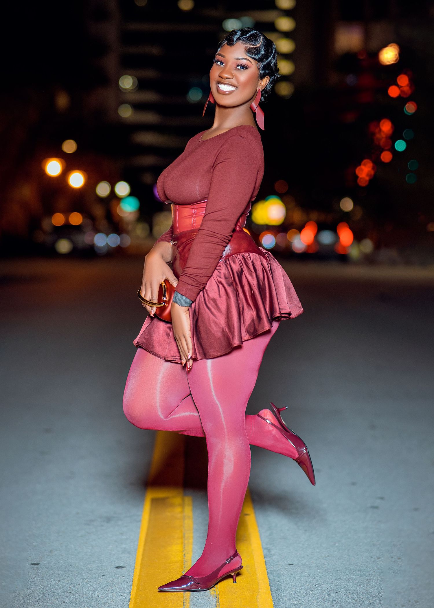 Person wearing burgundy outfit with ruffles strikes fashionable pose against night city backdrop.