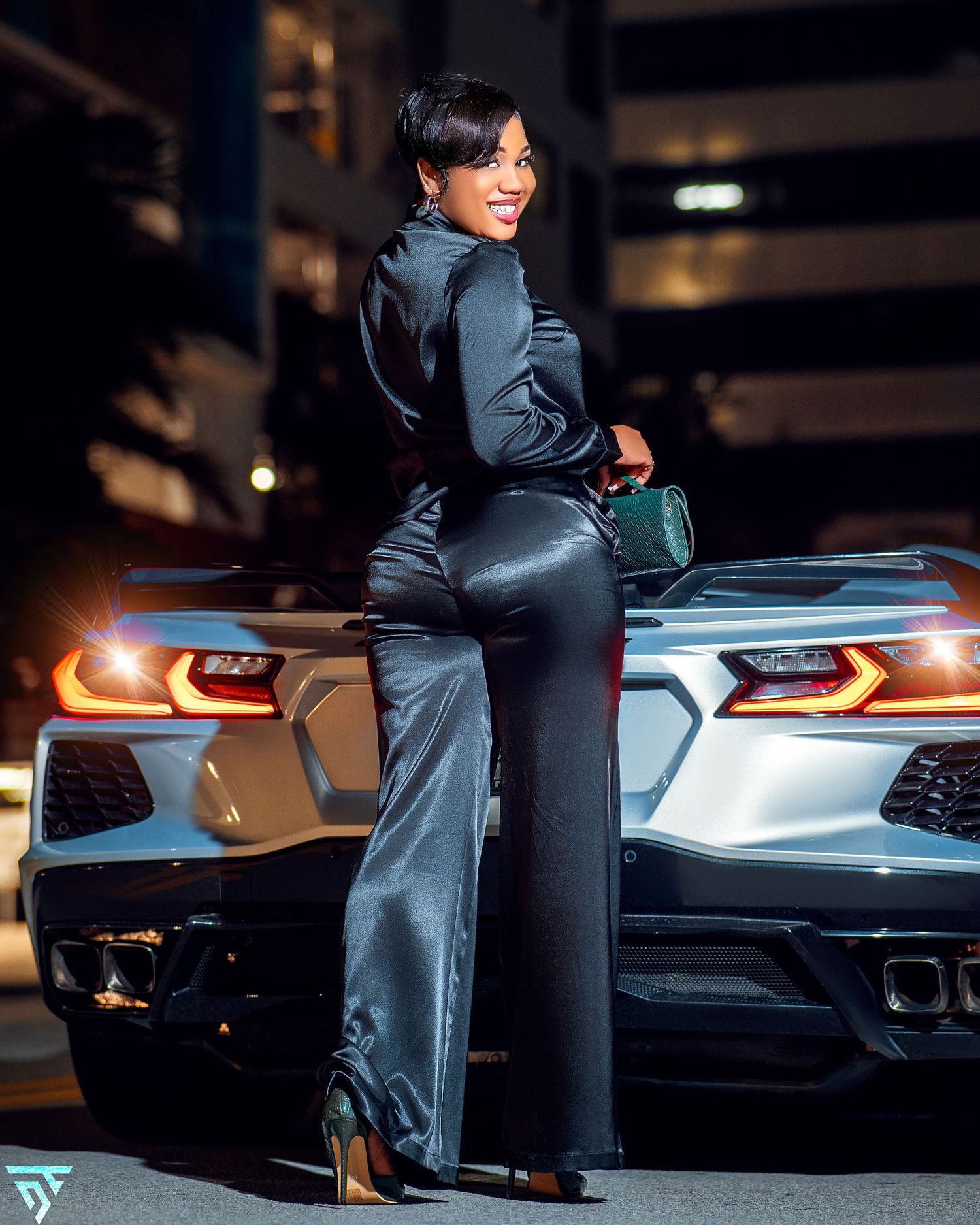 Silver sports car with illuminated taillights parked at night with person sitting on trunk.