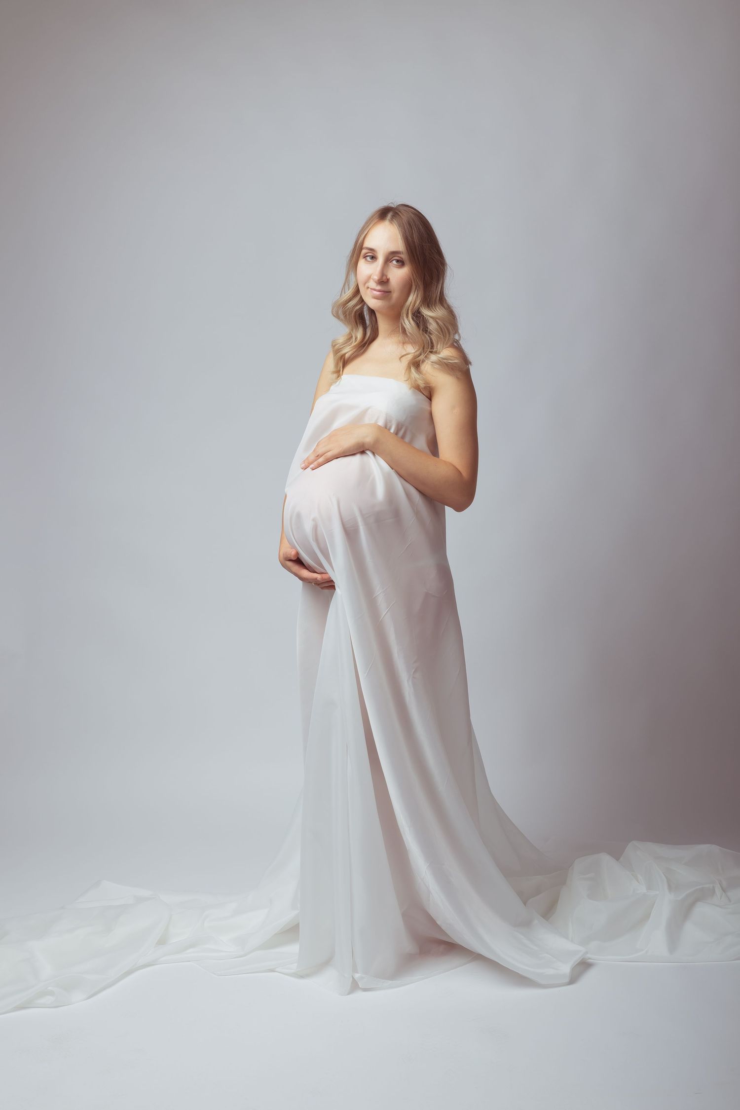 Ethereal maternity portraits with flowing white fabric against light grey backdrop.