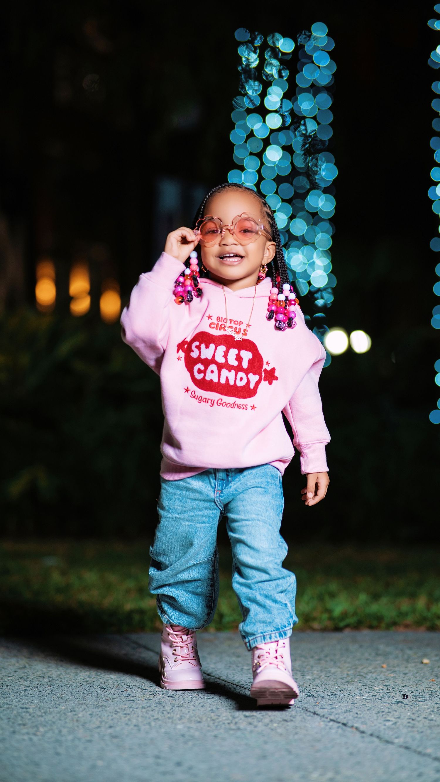 Toddler in pink Sweet Candy sweatshirt and jeans smiles while standing outdoors.