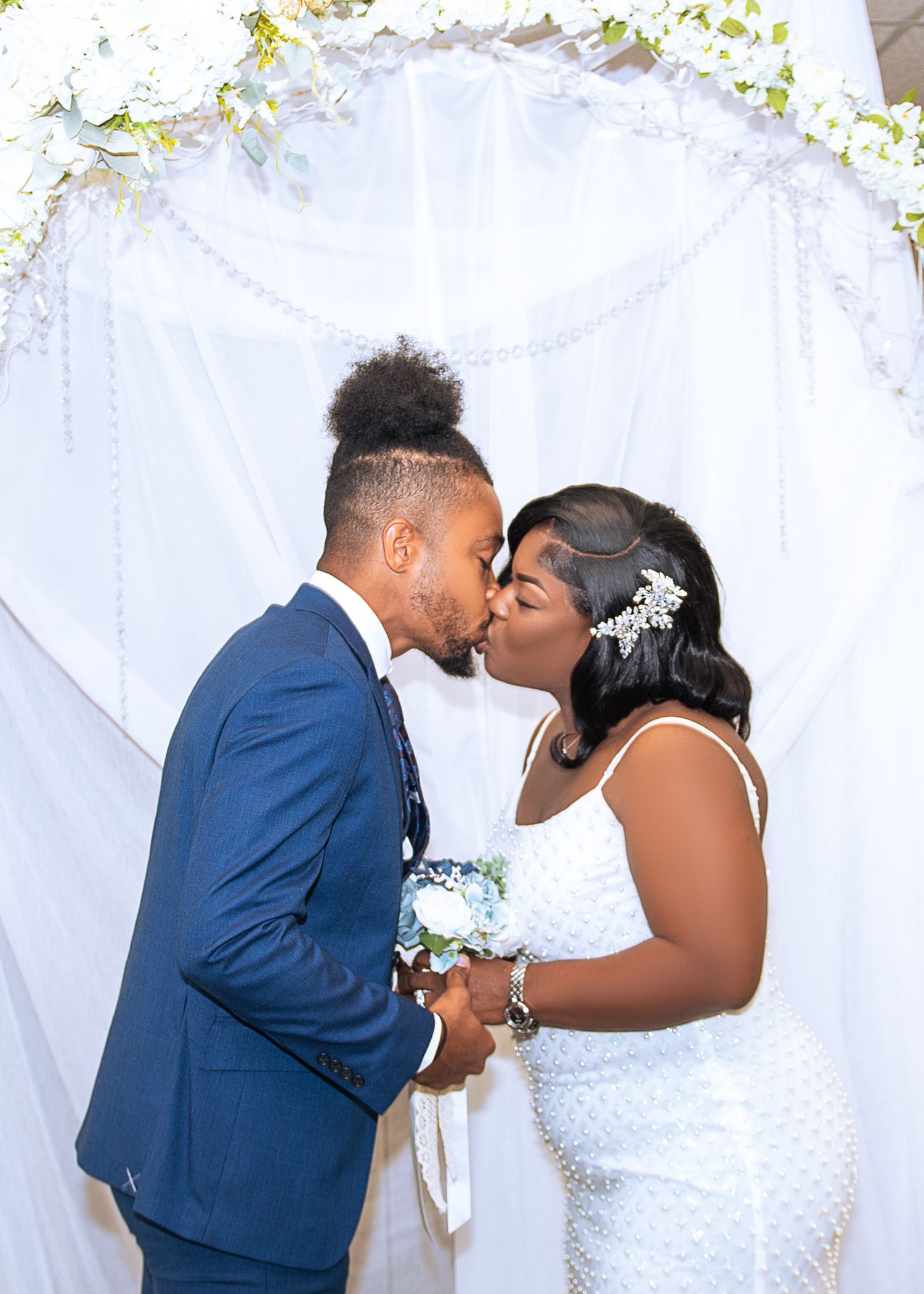 A couple shares romantic wedding day kisses against a white floral backdrop.