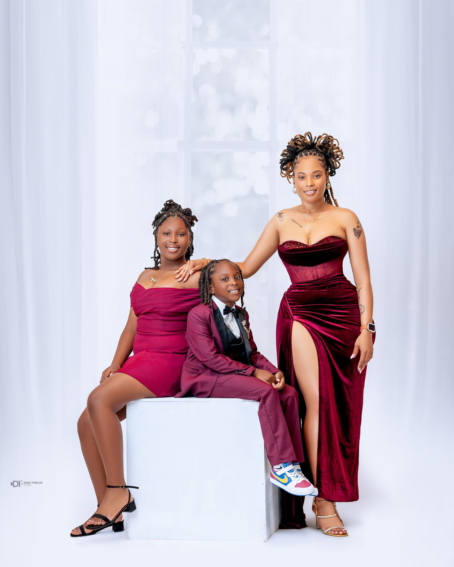 Three people in elegant burgundy outfits pose together in a bright studio setting for a formal portrait.