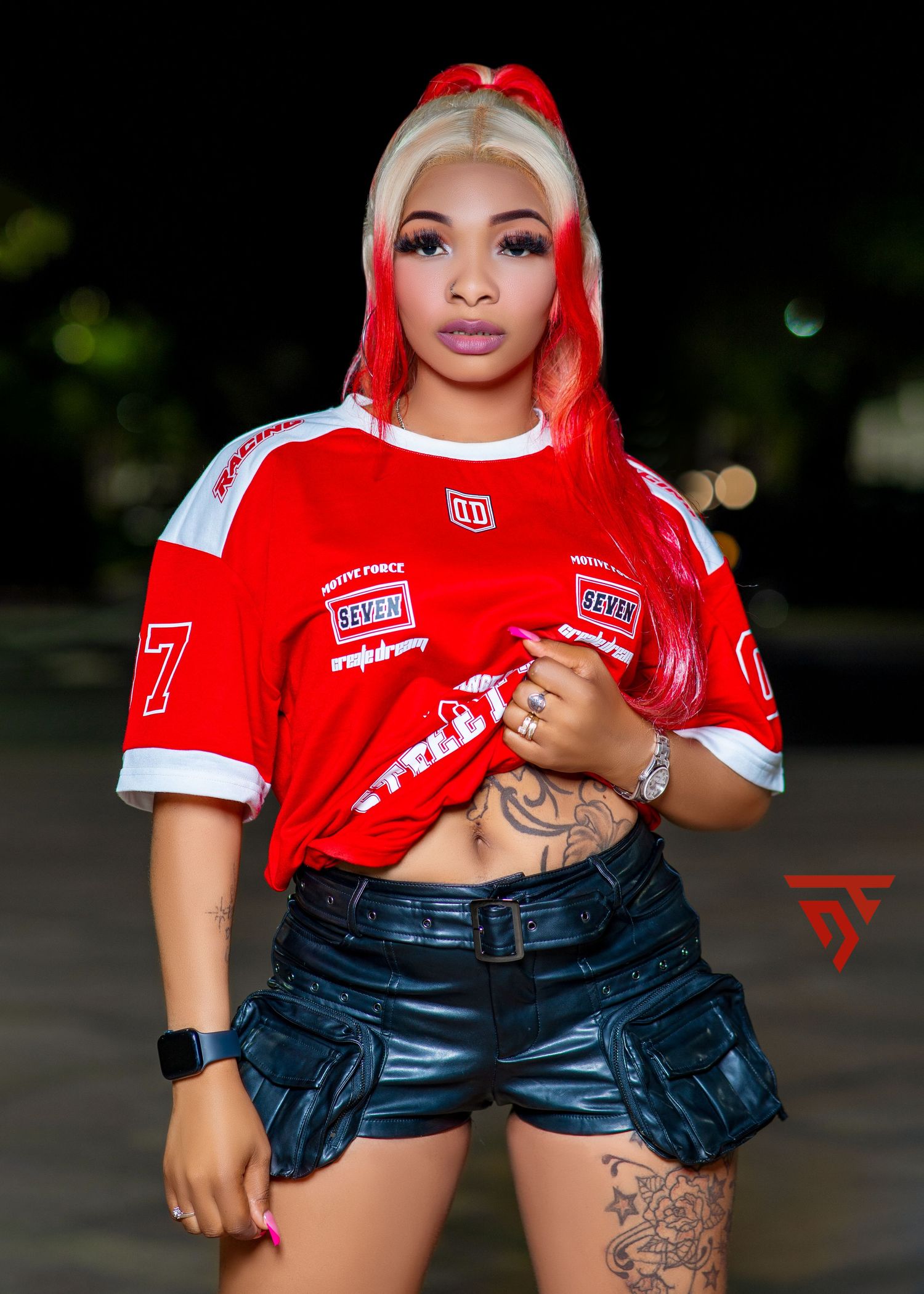 Fashion model wearing a red t-shirt and dark shorts poses in multiple casual poses outdoors at night.