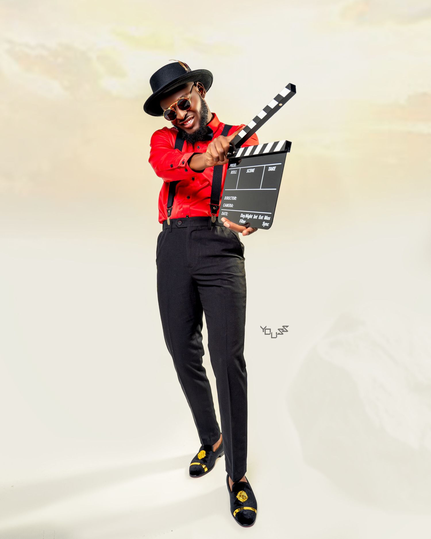 Creative photoshoot with person in red shirt and black pants holding movie production clapperboard.