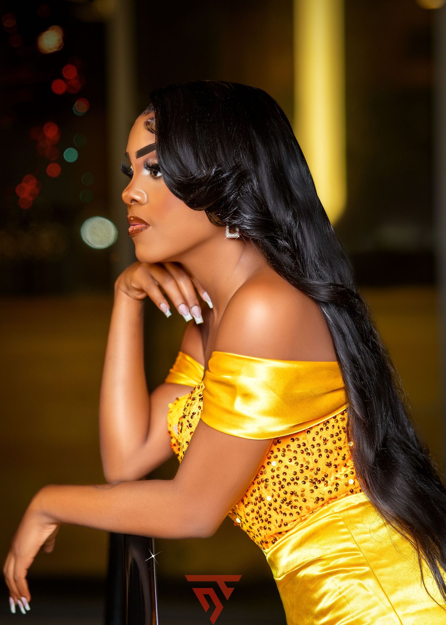 Elegant portrait in yellow satin gown with long flowing hair against night lights.