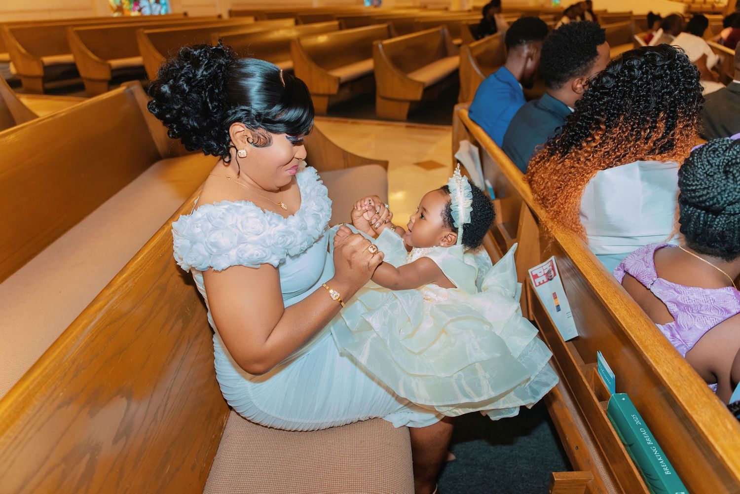 Tender moment captured in church pew with light blue dress and white formal attire.