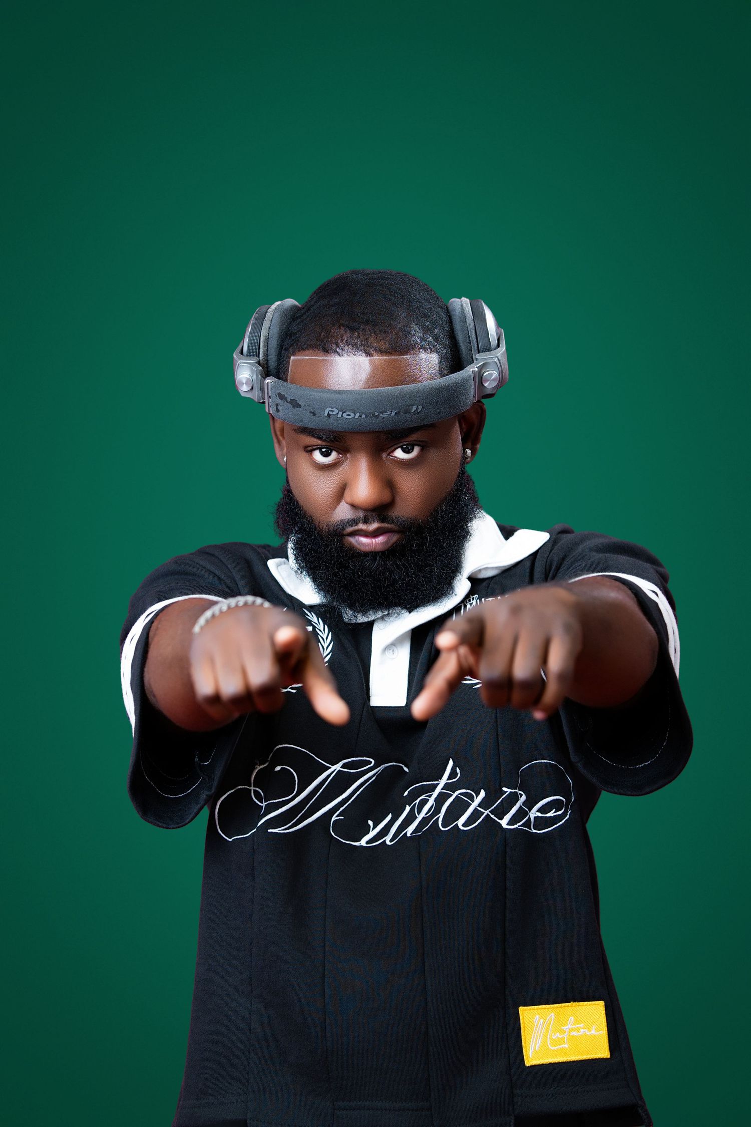 Bearded Black man in black hoodie with VR headset pointing at camera against green background.
