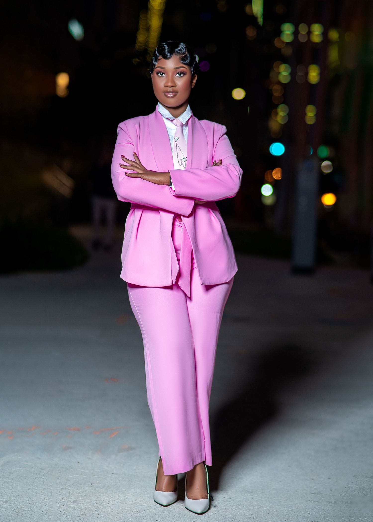 Person in pink business attire poses professionally against evening cityscape.