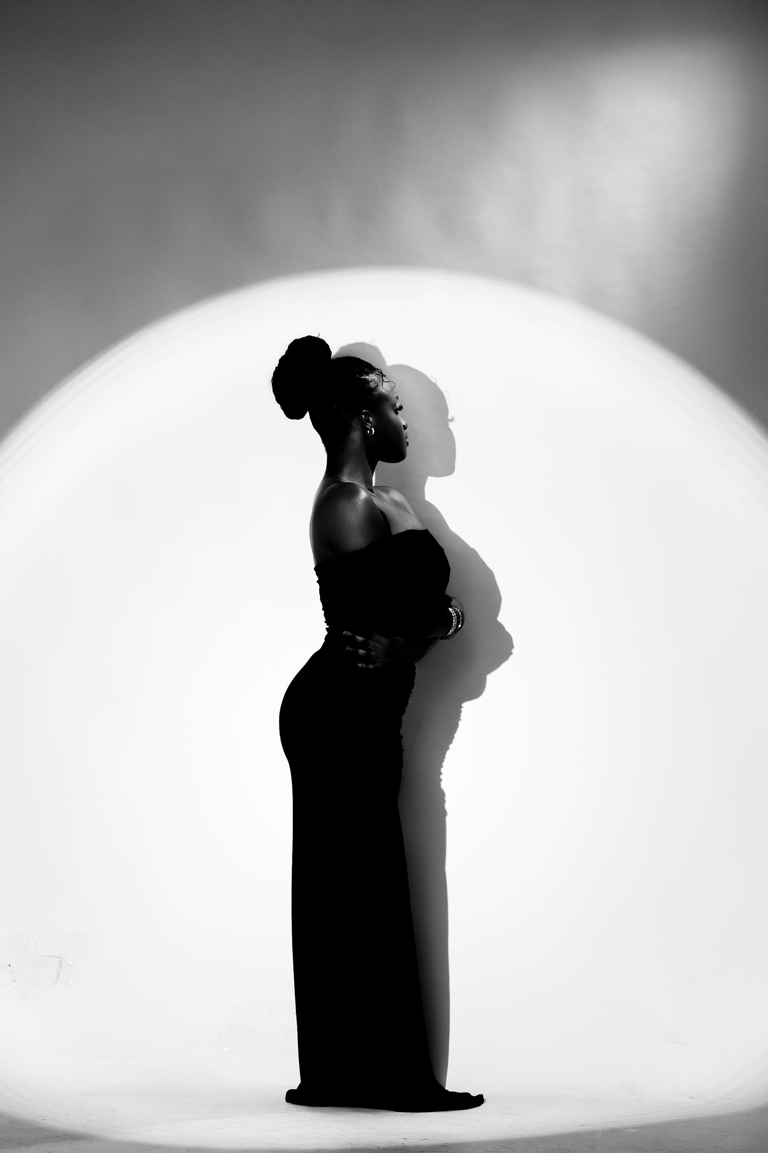 Black and white silhouette of a woman in an elegant gown posed against a glowing circular backdrop.