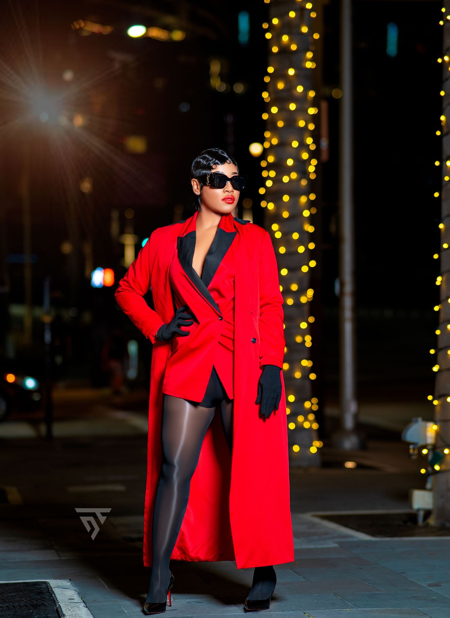 Stylish red coat and sunglasses captured in urban nighttime setting with string lights.